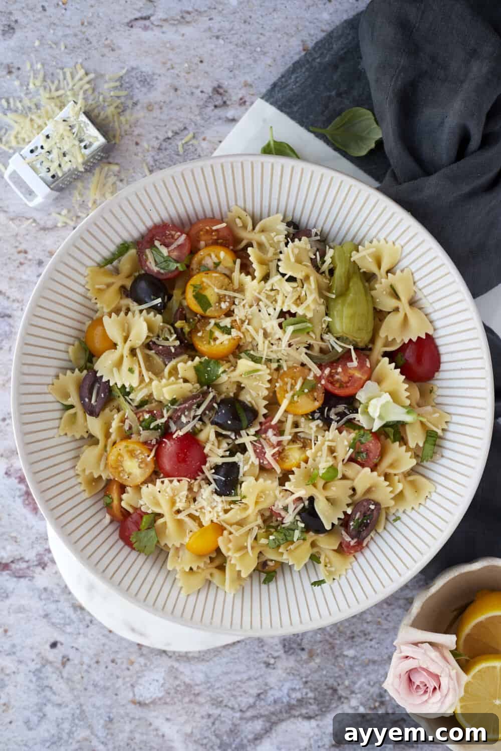 Overhead image of warm Italian pasta salad in a bowl topped with shaved Parmesan cheese and fresh basil