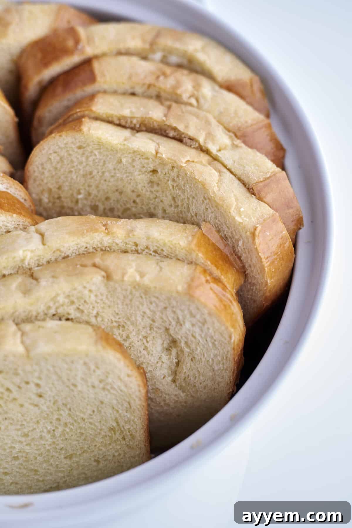 Slices of brioche bread neatly arranged in a white baking dish, prepared and ready to be immersed in custard and baked into a mouthwatering casserole.