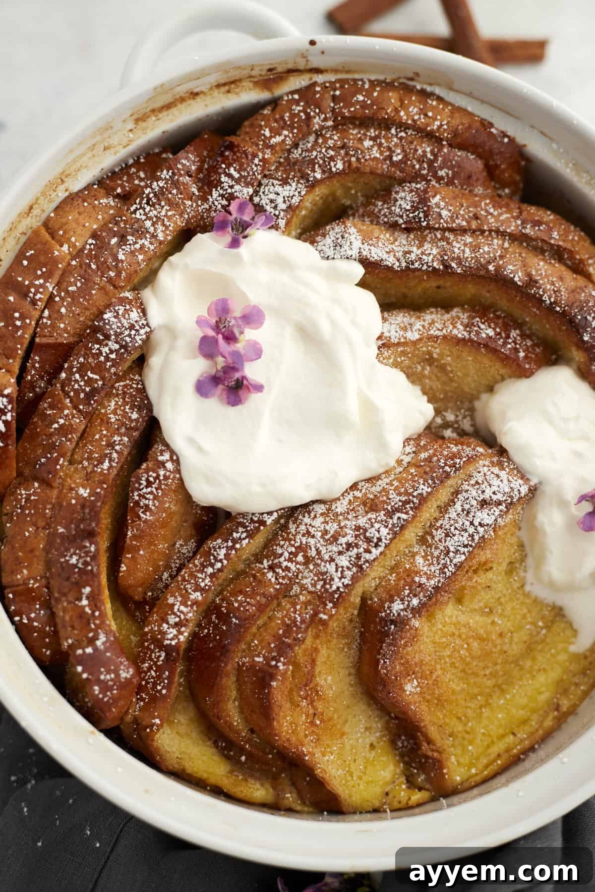 A beautiful close-up of a white baking dish showcasing baked cinnamon French toast, adorned with delicate powdered sugar and rich mascarpone cheese, ready for an indulgent brunch.