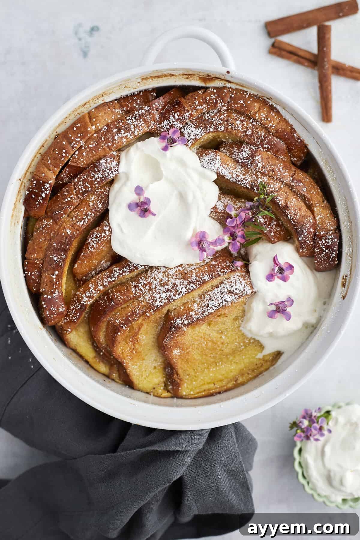 A white baking dish with baked cinnamon French toast topped with powdered sugar and mascarpone cheese, ready to serve.