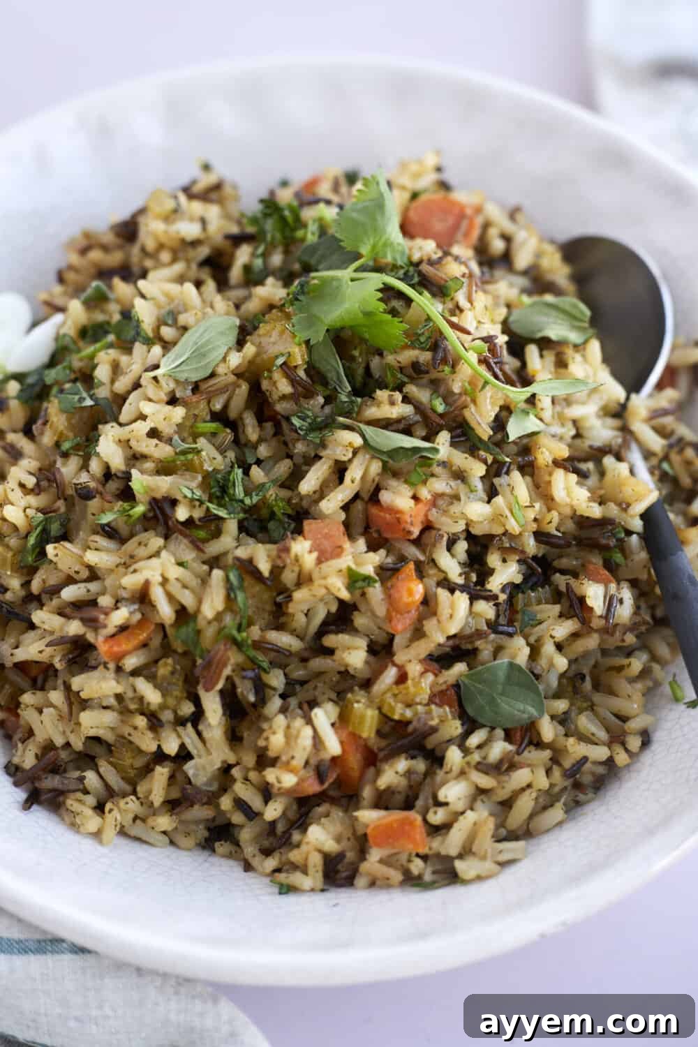 A close-up view of a serving of seasoned rice, generously topped with fresh green herbs, presented in a bowl with a spoon alongside.