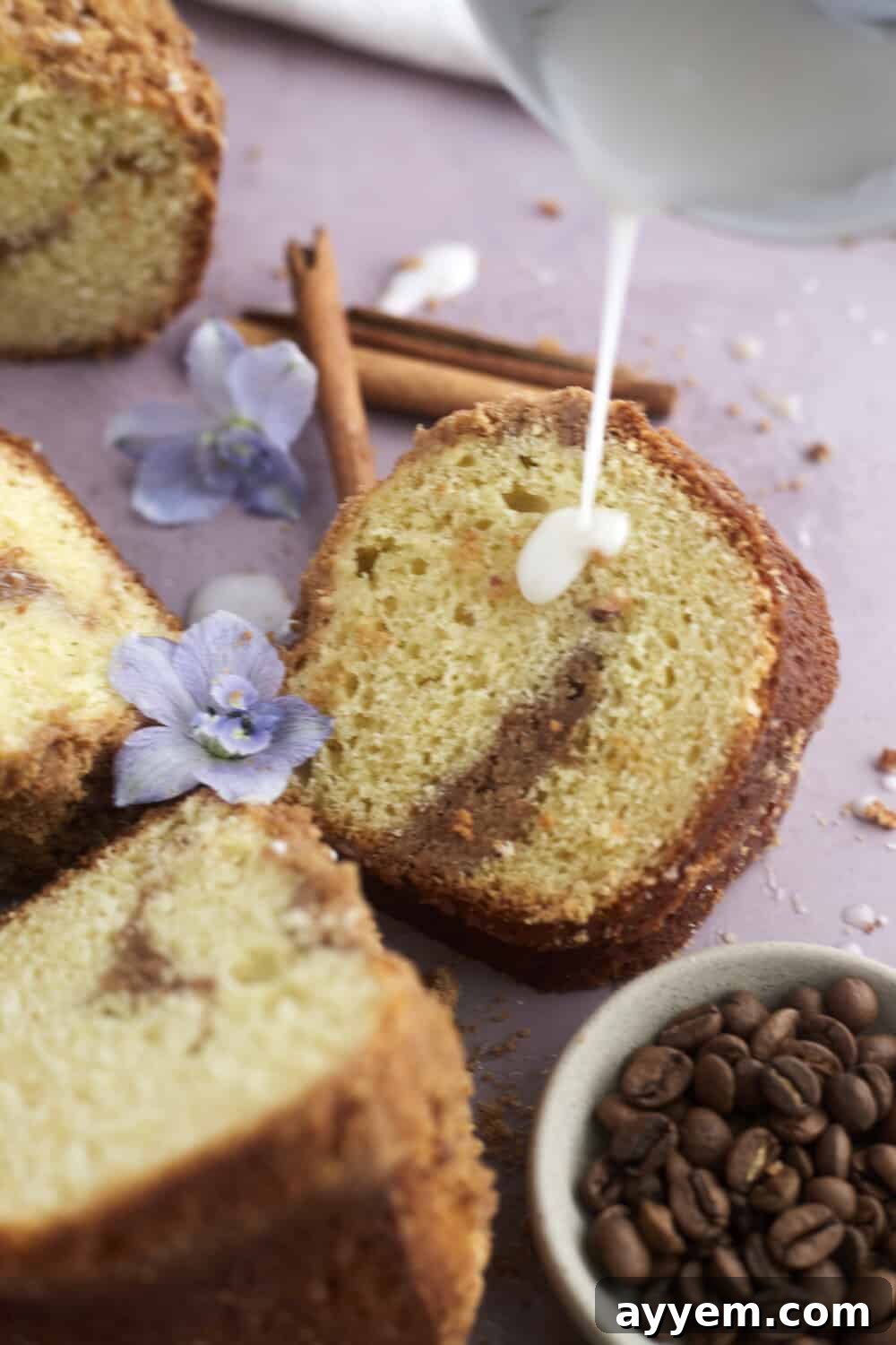 A mesmerizing shot of a slice of sour cream coffee cake, with the decadent cream cheese glaze gracefully being drizzled over the top.
