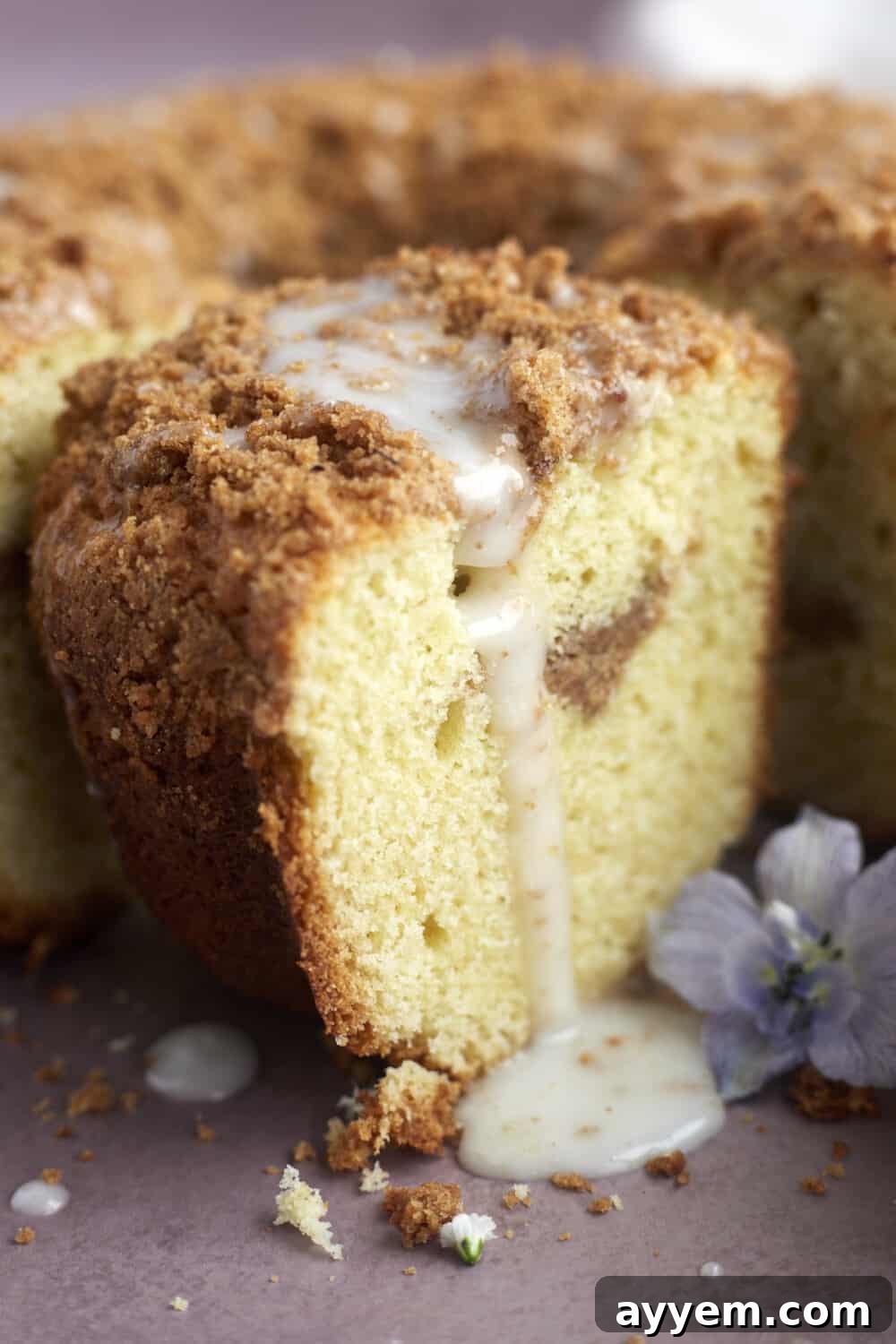 A close-up view of a slice of sour cream coffee cake, showing the rich texture, streusel layers, and tempting glaze dripping down its sides.