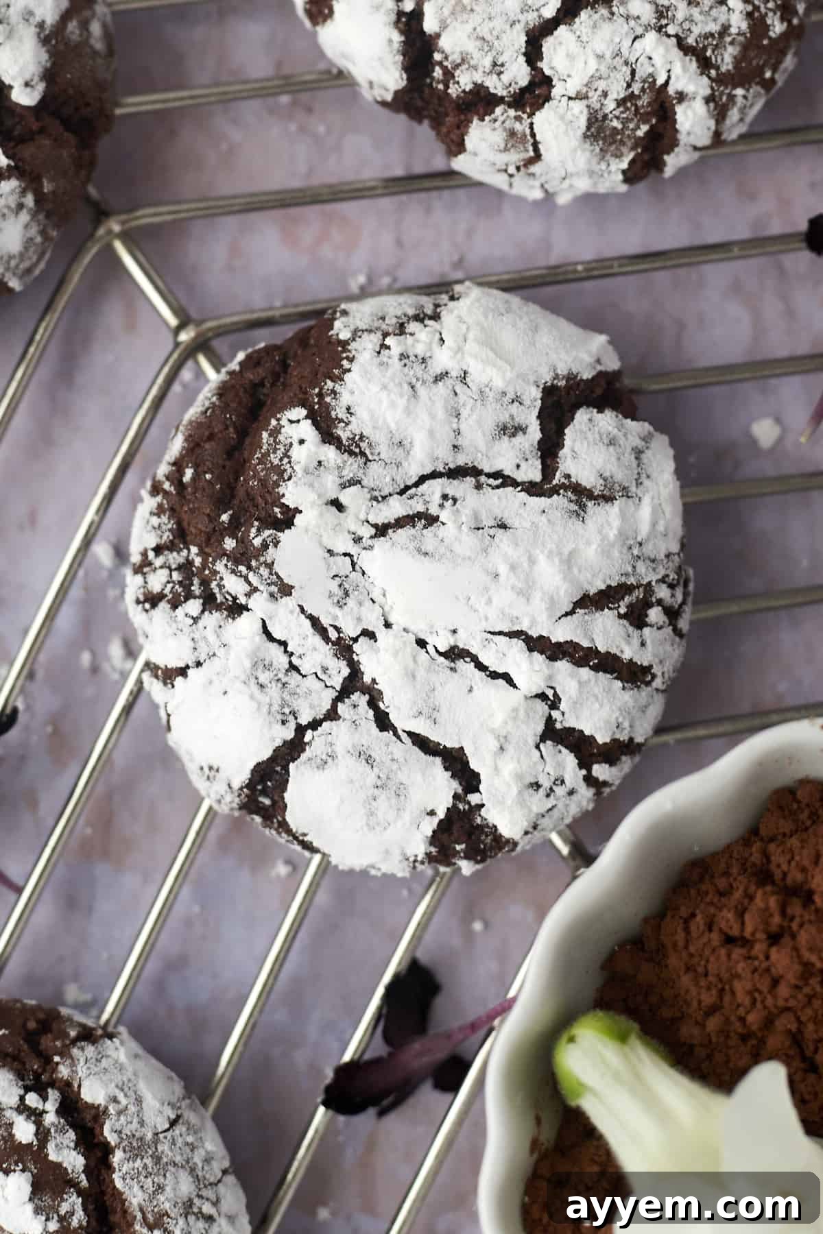A perfectly baked chocolate crinkle cookie on a wire cooling rack, showcasing its iconic powdered sugar coating and fudgy interior.