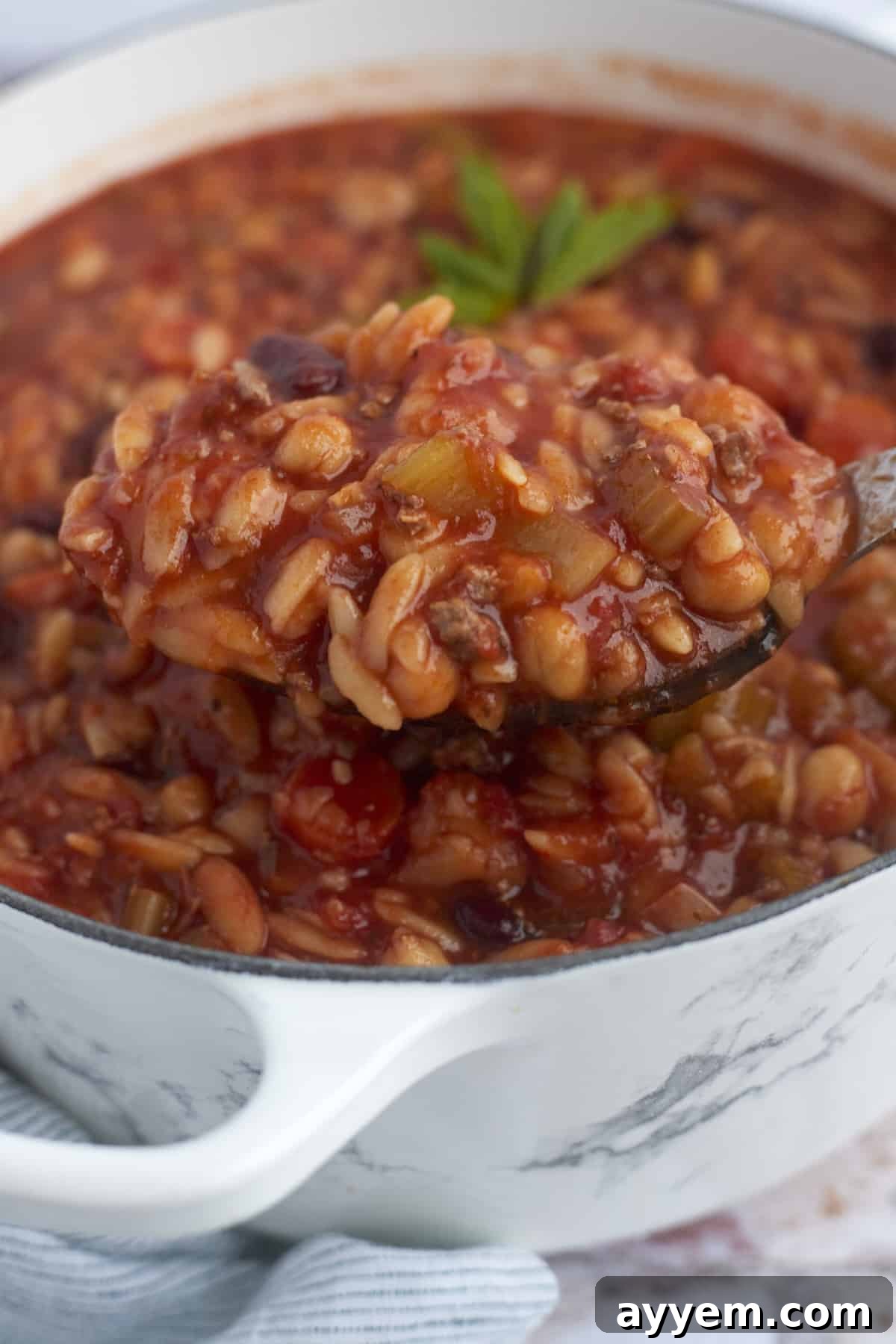 A generous spoonful of rich Pasta e Fagioli being lifted from a large pot, steaming invitingly.