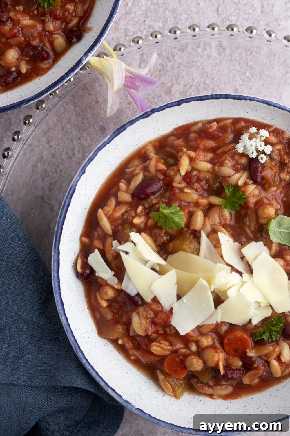 A beautifully presented bowl of creamy pasta and beans soup, generously topped with shaved Parmesan cheese, highlighting its comforting and indulgent appeal.