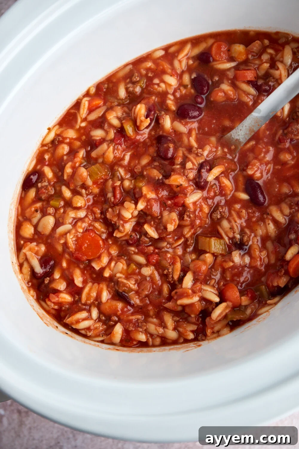 An overhead shot of a slow cooker filled with ready-to-serve pasta and beans soup, indicating a generous and comforting meal.