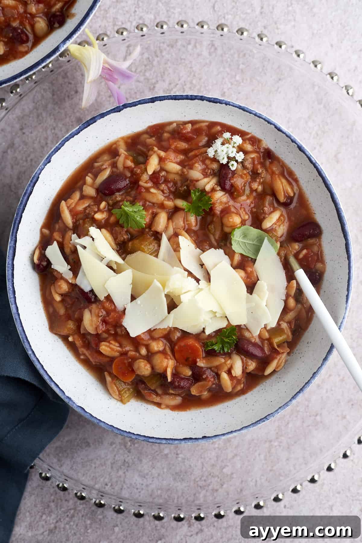 A bowl of Slow Cooker Pasta and Beans Soup (Pasta E Fagioli) topped with Parmesan cheese, ready to be enjoyed.