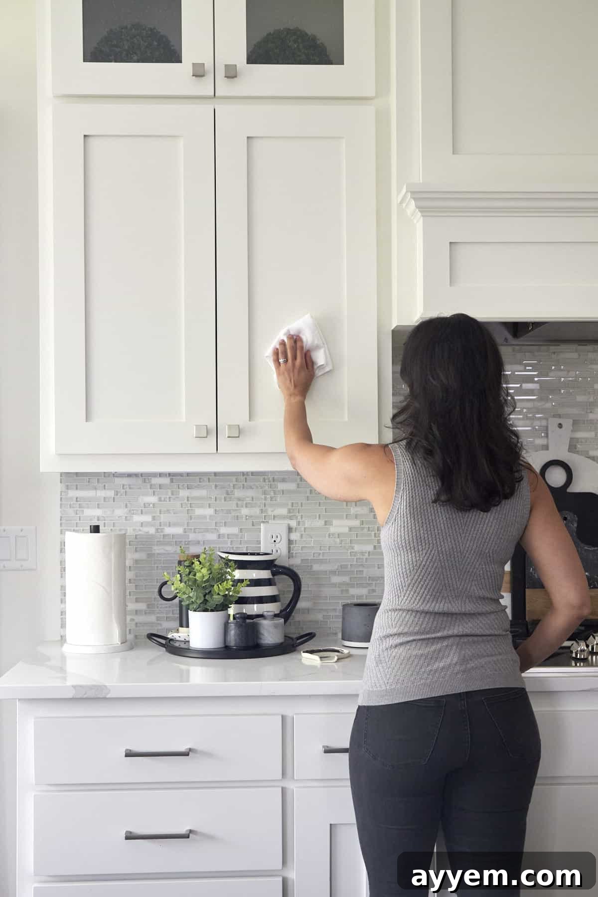 A woman using a microfiber cloth to wipe down kitchen cabinets. 