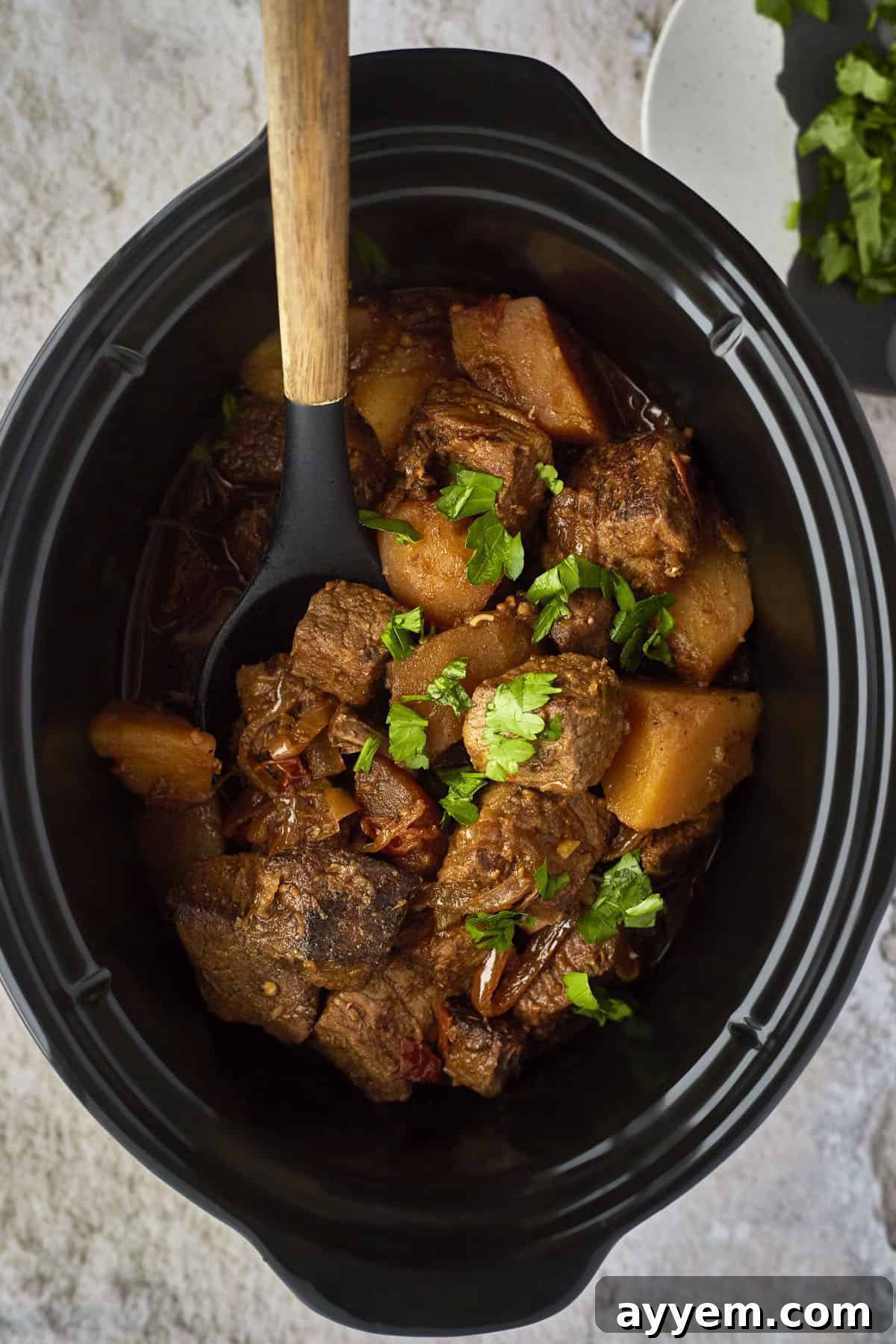 Cooked beef stew with potatoes in a crockpot. 