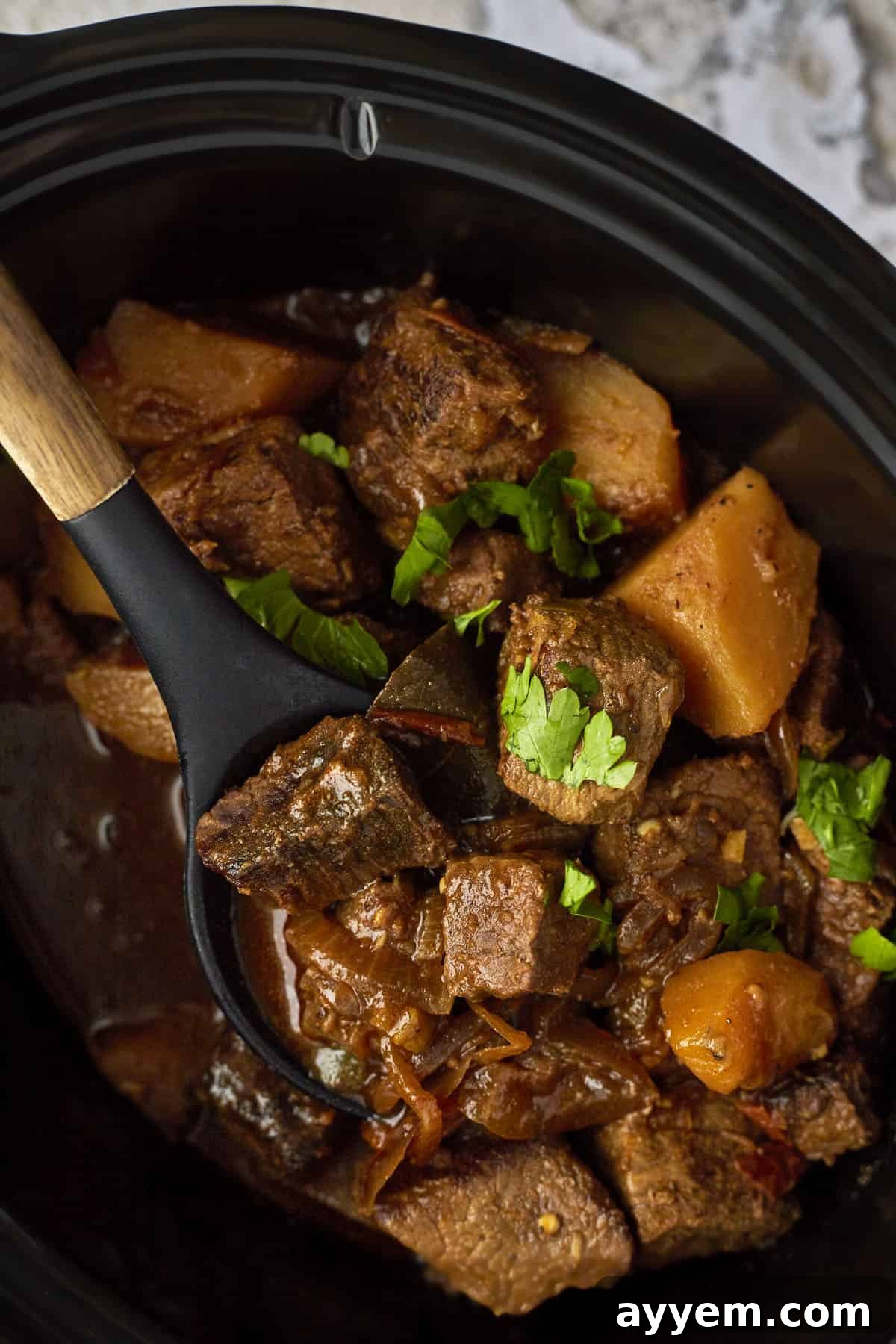 A spoon lifting a scoop of Middle Eastern beef stew from a crockpot. 