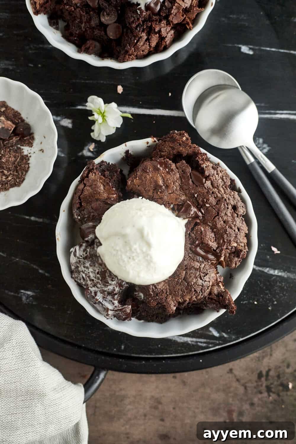 An overhead view of individual servings of Chocolate Hazelnut Skillet Brownie, each topped with a scoop of vanilla ice cream, presented in small white bowls with spoons on the side.