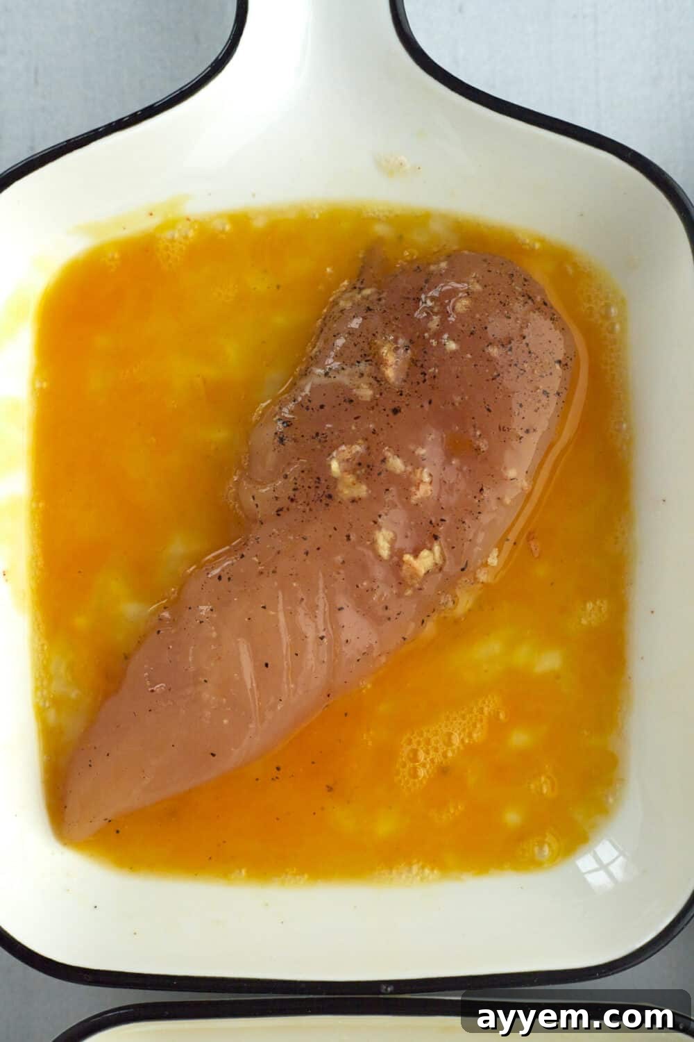 A chicken tender being coated in a whisked egg wash, part of the dredging process for crispy chicken.