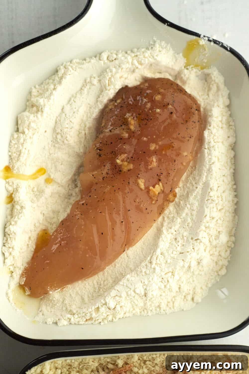 A chicken tender being dipped and coated in a seasoned flour mixture, the first step in creating a crisp breading.