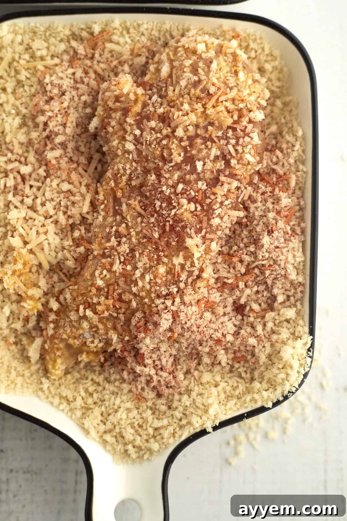 Raw chicken tender being coated thoroughly with a breadcrumb and Parmesan cheese mixture.