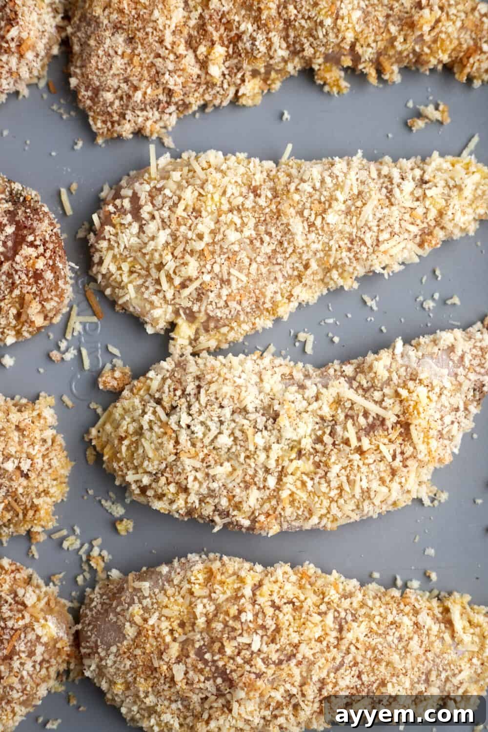 A baking sheet filled with raw, panko-breaded chicken tenders, ready for oven baking.