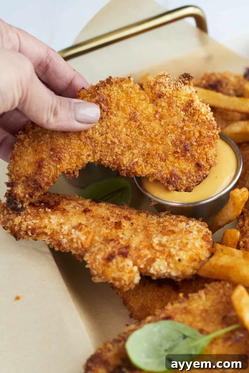 A crispy breaded chicken tender being dipped into a bowl of creamy honey mustard sauce, showcasing its golden crust.