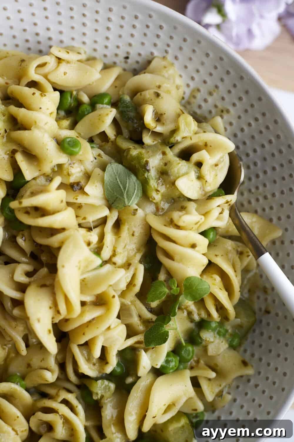 A close-up view of creamy pesto pasta, showcasing the perfectly coated rotini pasta with visible bits of asparagus, zucchini, and peas. The dish looks rich and inviting.