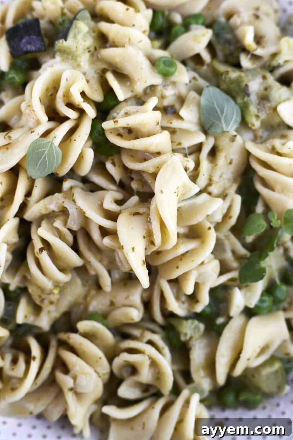 A vibrant close-up of creamy pesto pasta, highlighting the fresh asparagus, tender zucchini, and green peas intertwined with the rotini pasta, all coated in a rich pesto sauce. Perfect for a healthy meal.