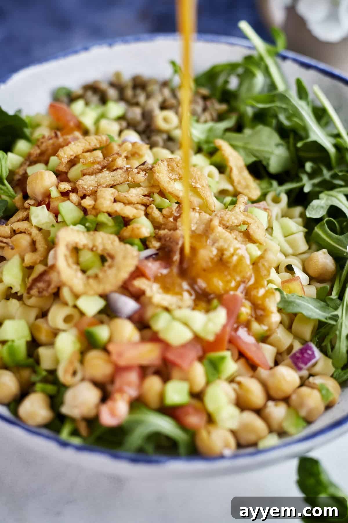 A mixing bowl filled with fresh salad ingredients, including arugula, tomatoes, cucumbers, red onion, and chickpeas, before dressing.