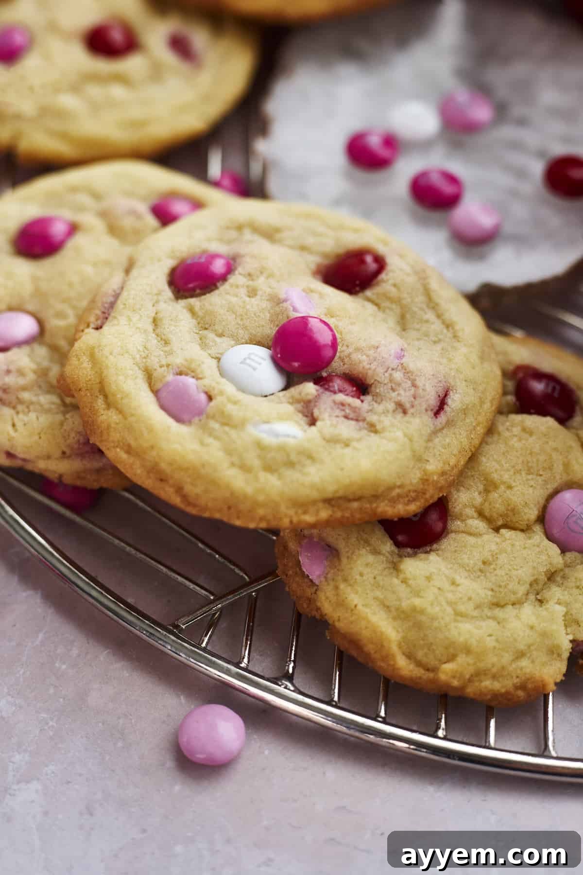 Freshly baked Valentine's M&M cookies on a baking rack with a bowl of M&Ms