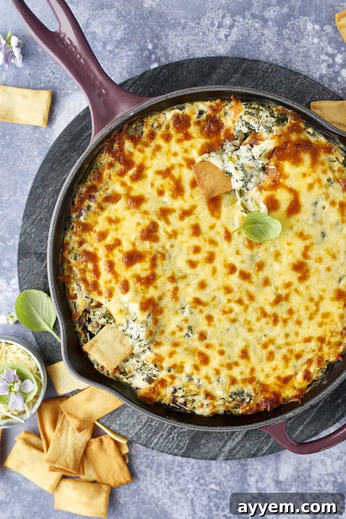 Warm, Cheesy Spinach Olive Dip in a skillet, garnished with fresh herbs, ready to be served with pita bread and vegetables.
