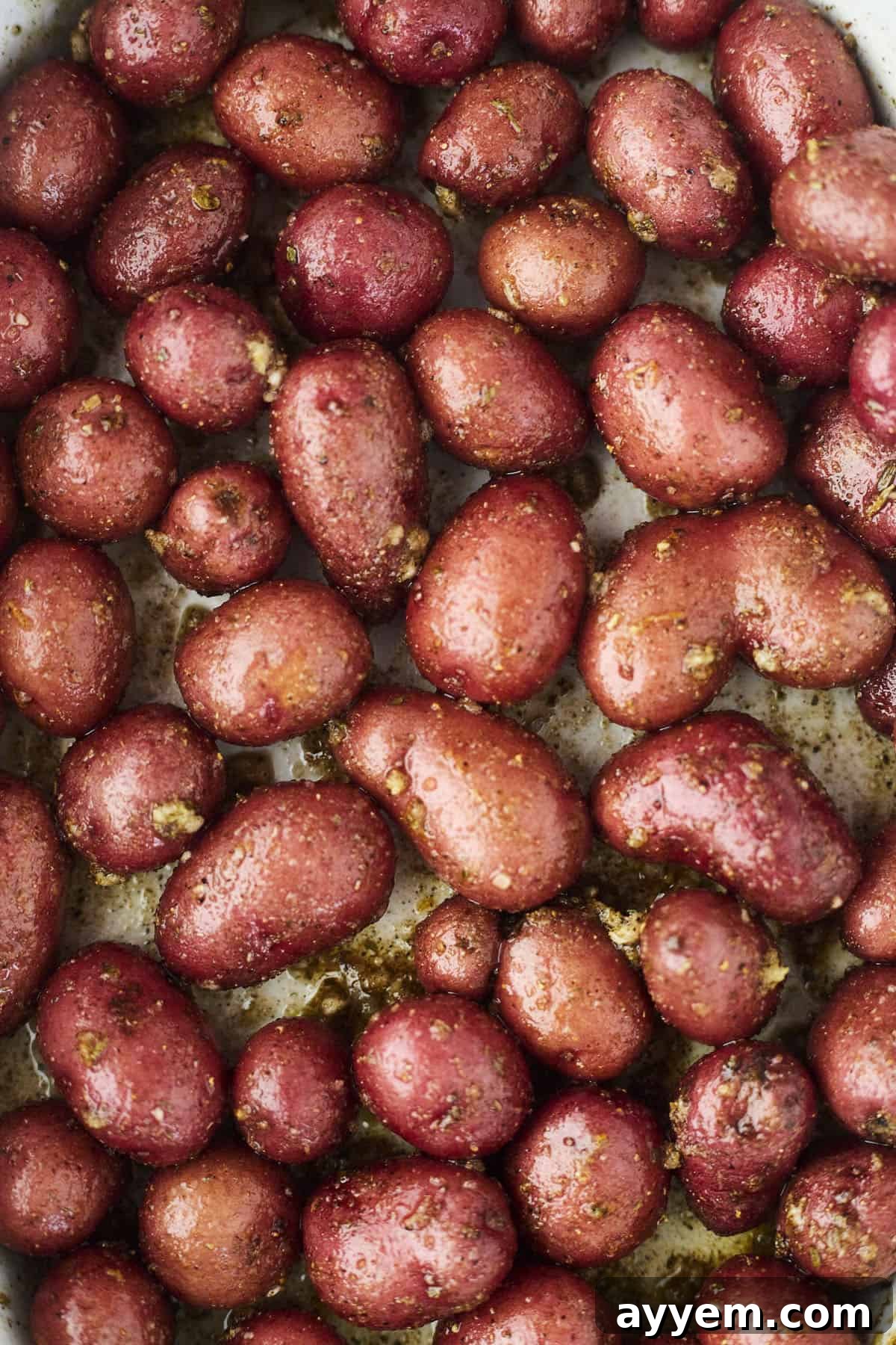 Red potatoes, uniformly cubed and glistening with olive oil and Greek spices, spread in a single layer on a parchment-lined baking sheet, ready for roasting.