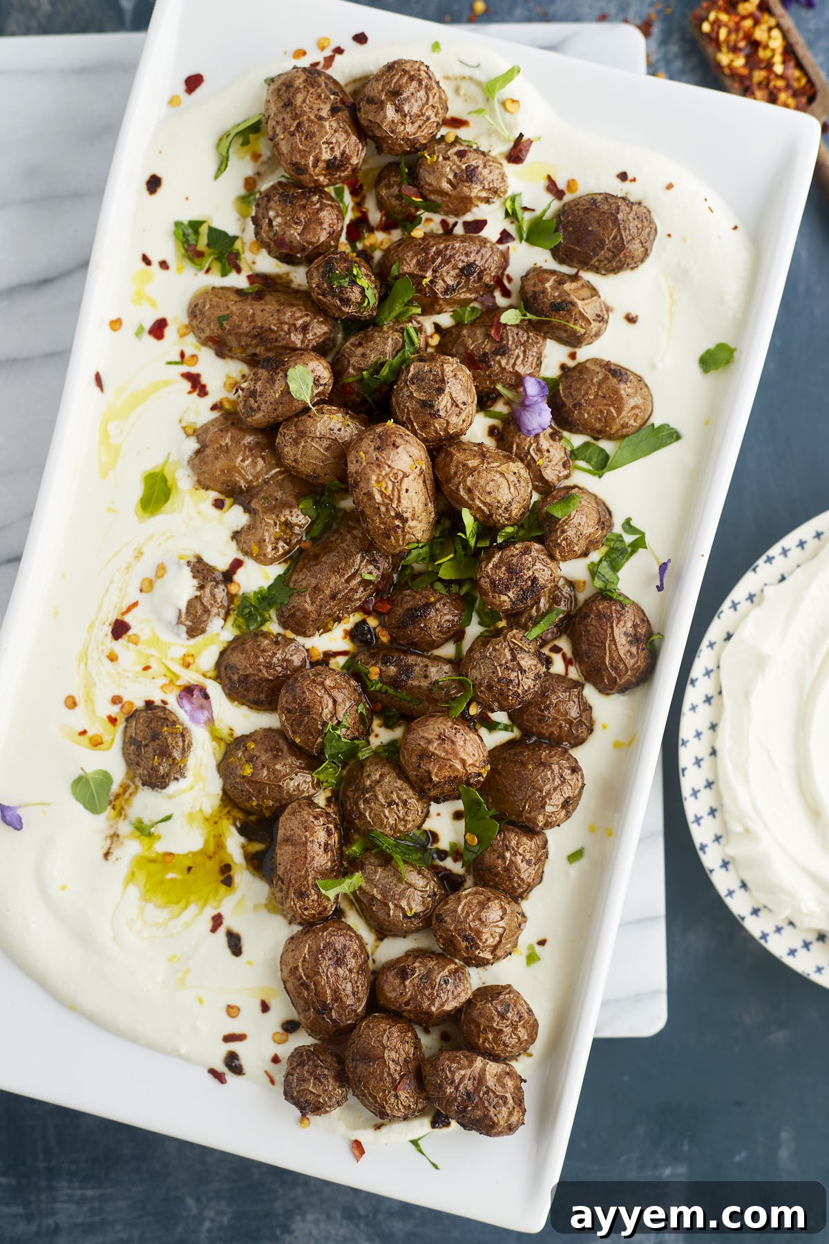A close-up view of roasted Greek potatoes resting on a bed of creamy whipped feta dip, garnished with fresh green herbs.