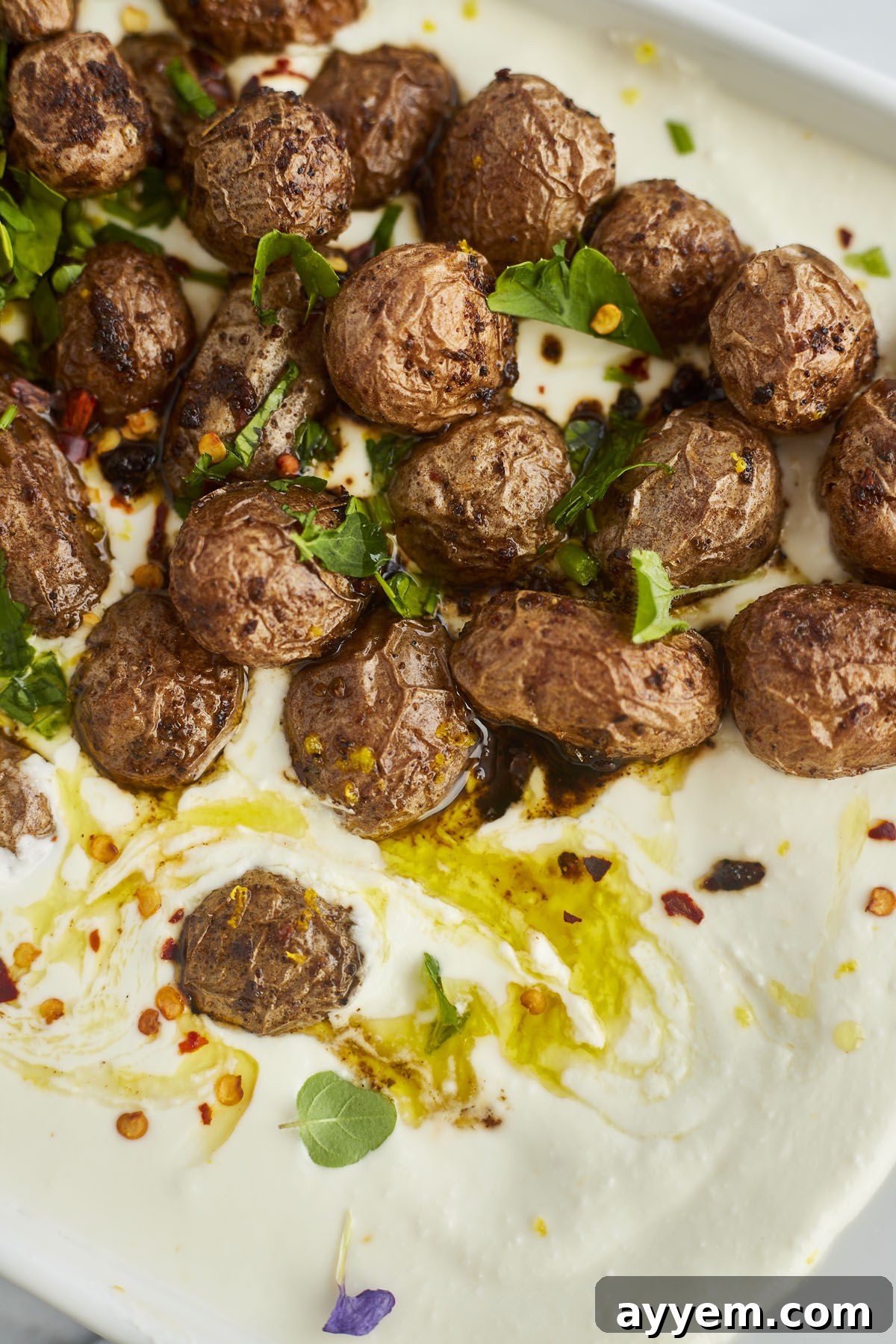 A close-up shot of crispy roasted potatoes atop a bed of creamy whipped feta, artfully drizzled with olive oil and sprinkled with red pepper flakes for an inviting finish.
