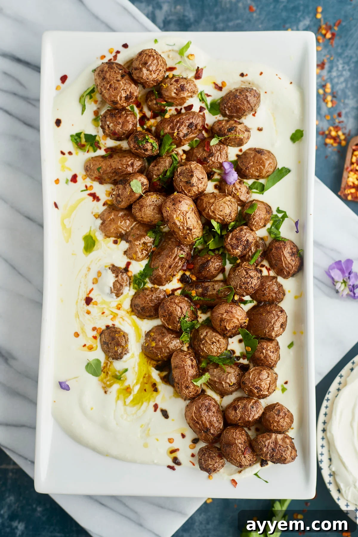 A platter showcasing golden-brown Greek roasted potatoes piled on a creamy whipped feta dip.