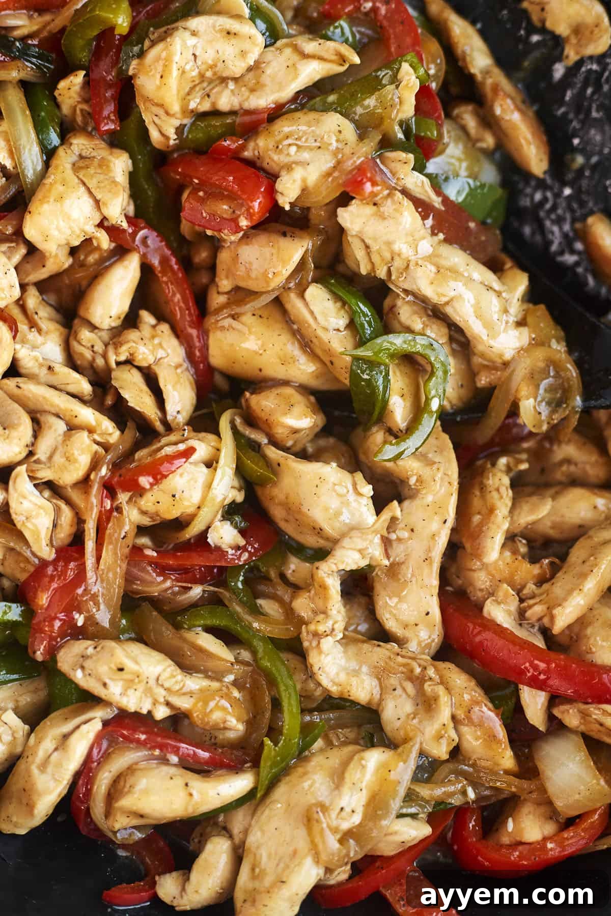 close up image of stir fry chicken, peppers, and onions in a skillet