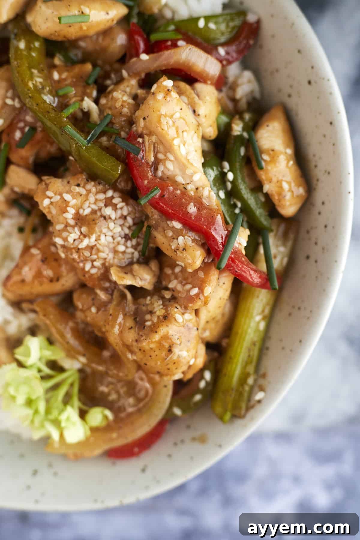 a bowl of black pepper chicken over rice topped with sesame seeds