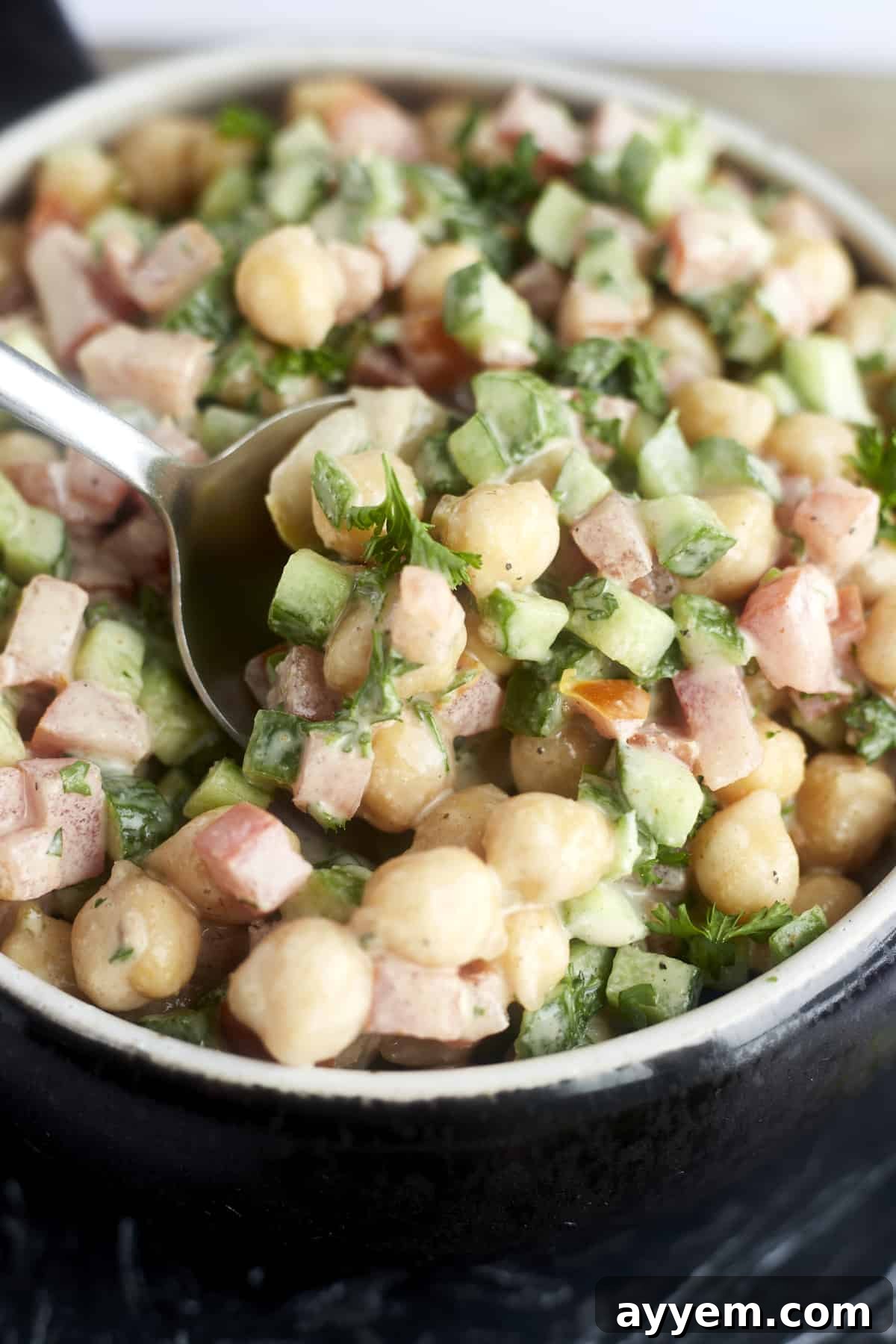 A close-up shot of a spoonful of chickpea, cucumber, and tomato salad, perfectly coated in a creamy tahini dressing.