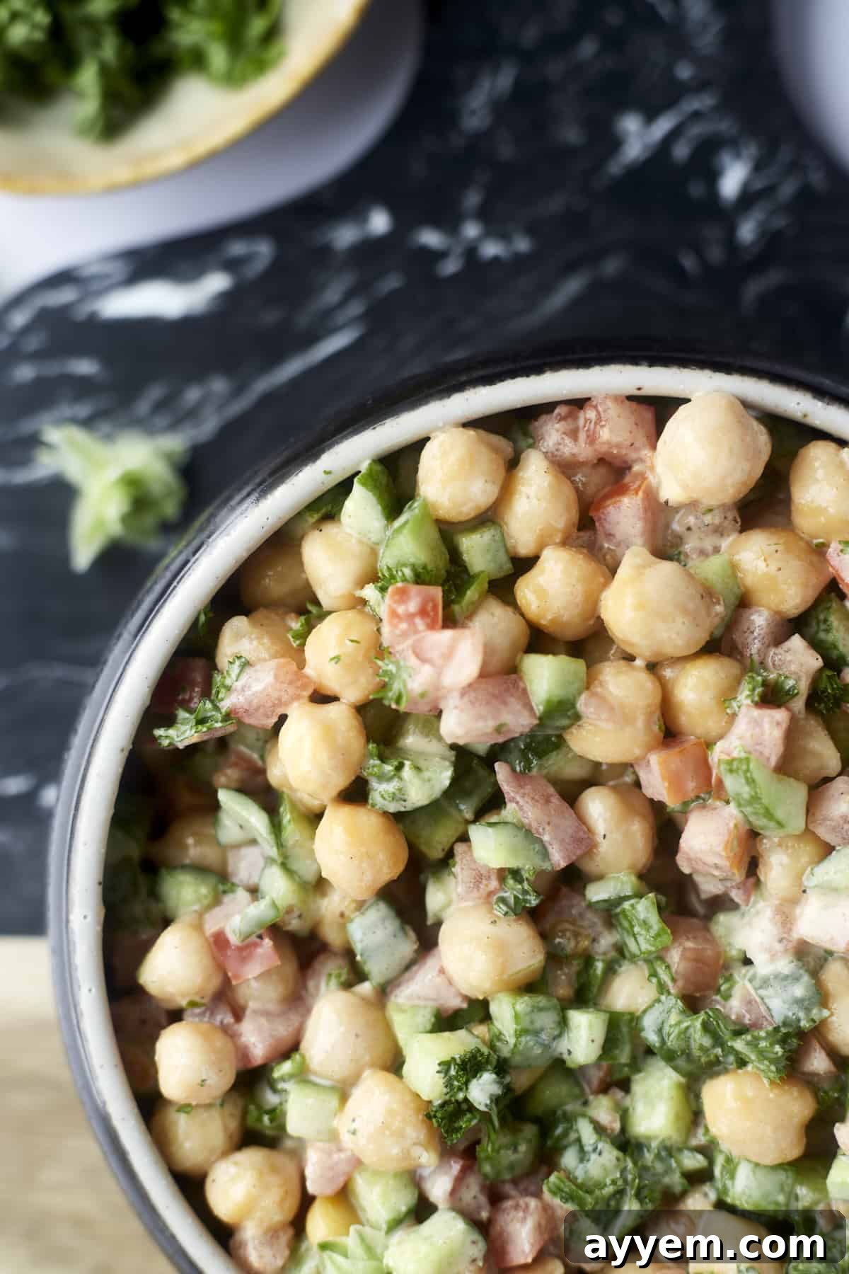A full bowl of chickpea and cucumber tahini salad, beautifully garnished with extra fresh parsley for a vibrant finish.