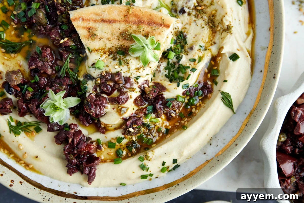 A serving platter with Za'atar Hummus and Olive Tapenade, garnished with fresh herbs and surrounded by various dippers.