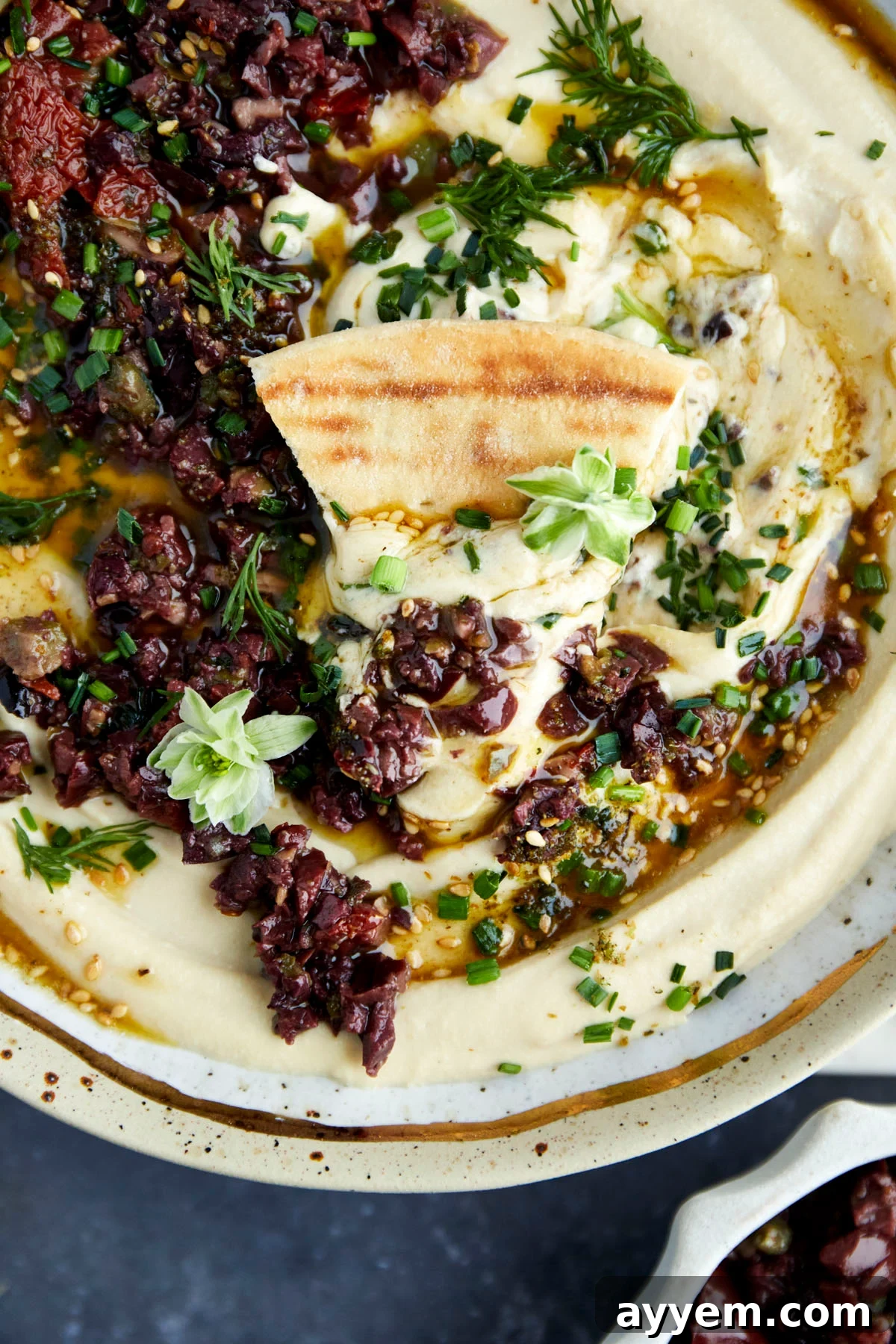 A close-up of a spoon scooping the Za'atar Hummus with Olive Tapenade, showing its rich texture and layers.