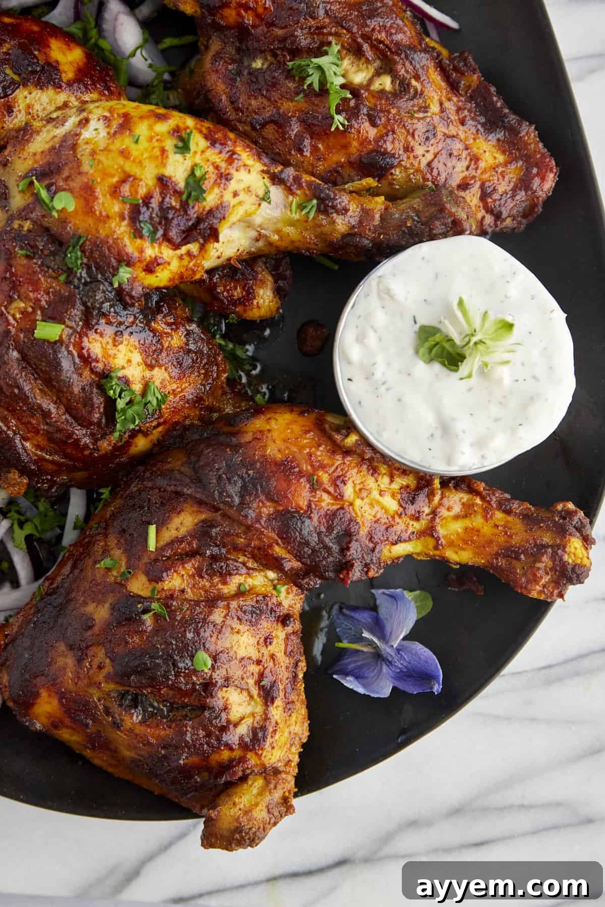 baked chicken tandoori legs on a plate with tzatziki on the side