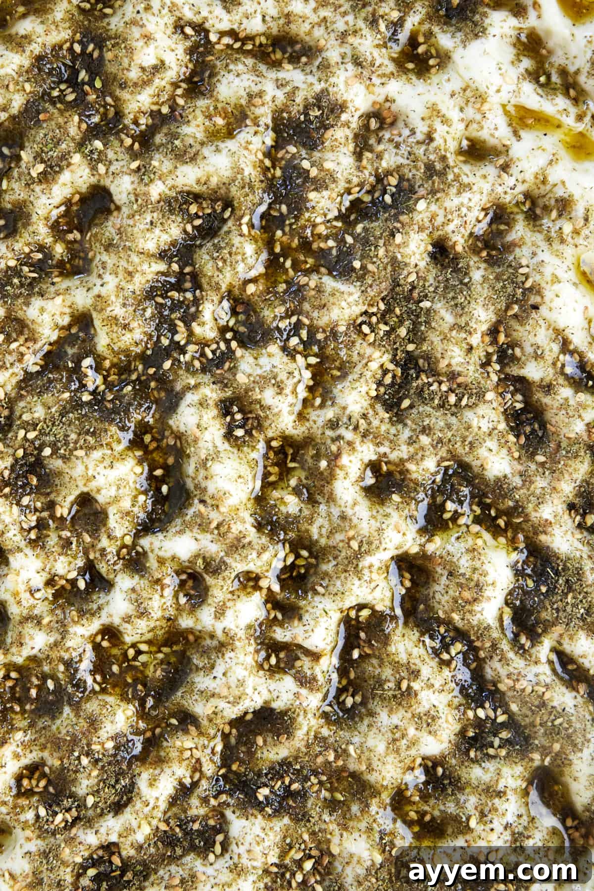 Unbaked quick focaccia recipe in a baking dish, topped with olive oil and za'atar seasoning, ready for the oven.