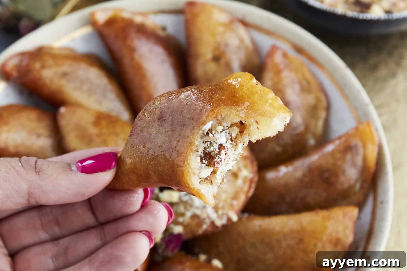 A hand holding a Qatayef with a bite taken out, revealing the sweet nut filling.