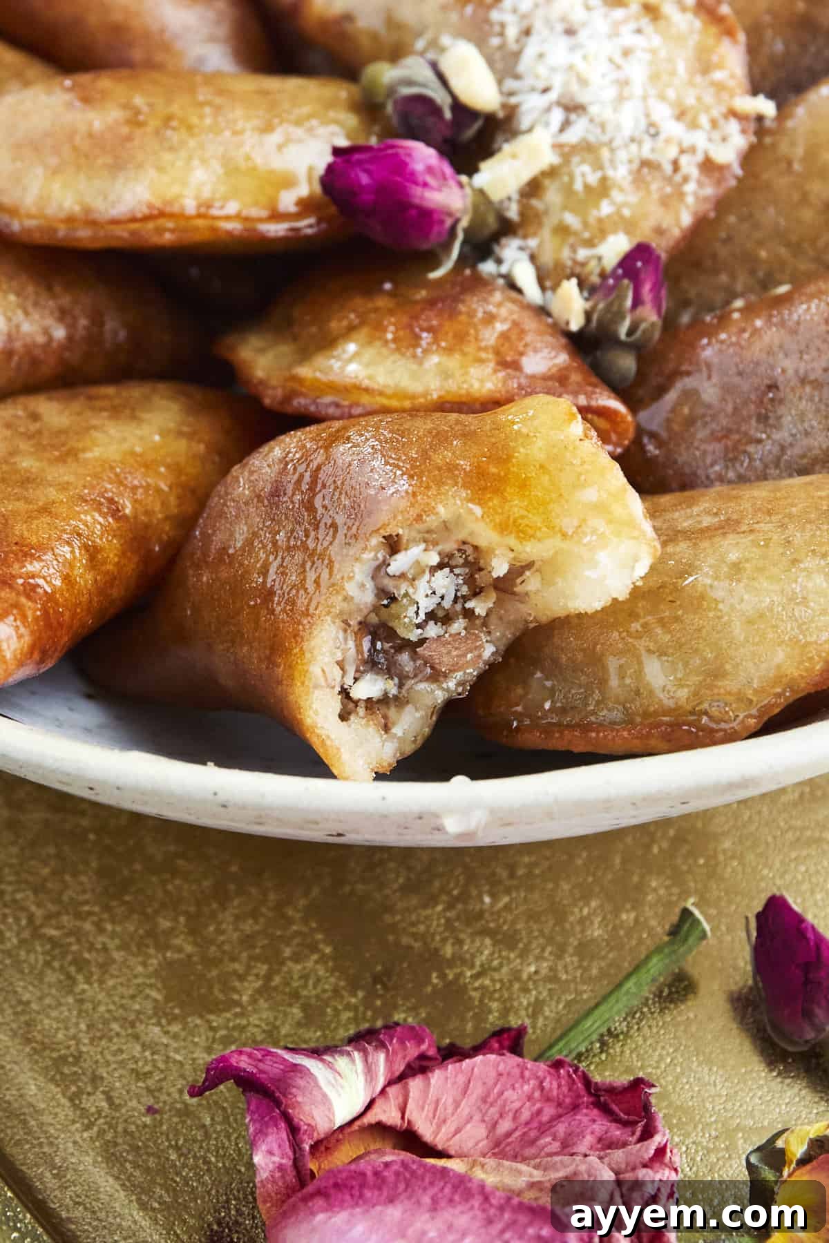 Close up image of a plate full of Qatayef with one piece missing a bite, revealing the nut filling and syrupy exterior.