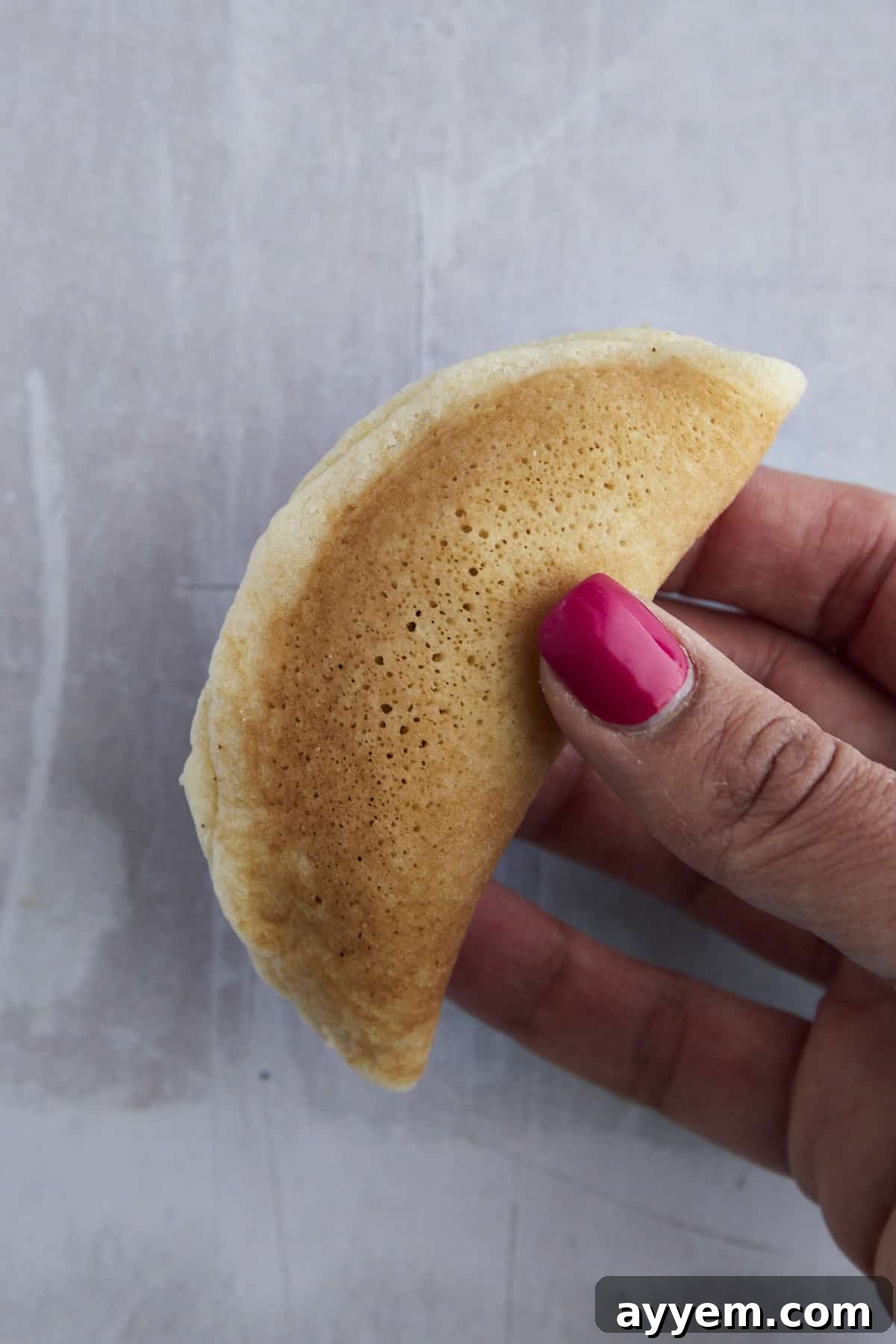 A hand holding a raw, stuffed Qatayef before frying.
