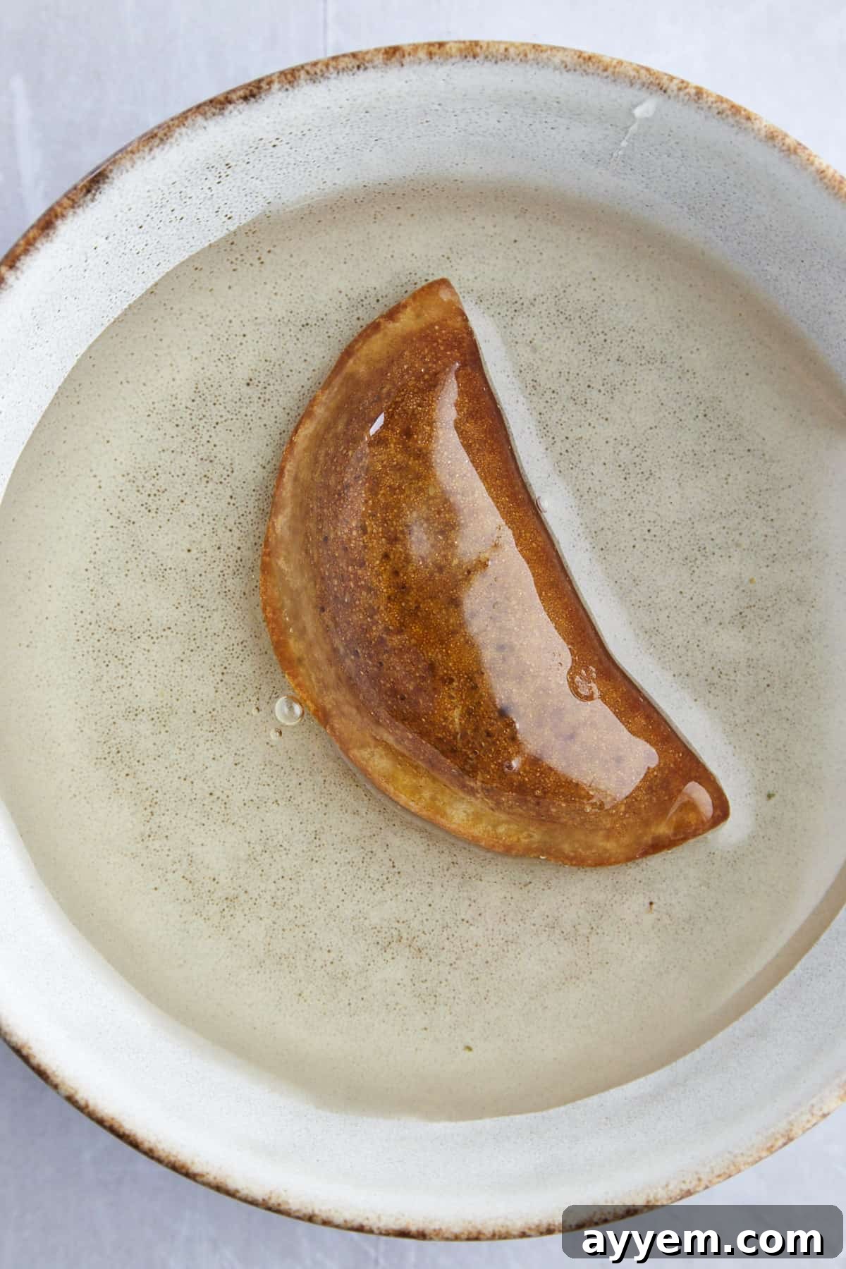 A single piece of fried Qatayef being dipped into a bowl of simple syrup.