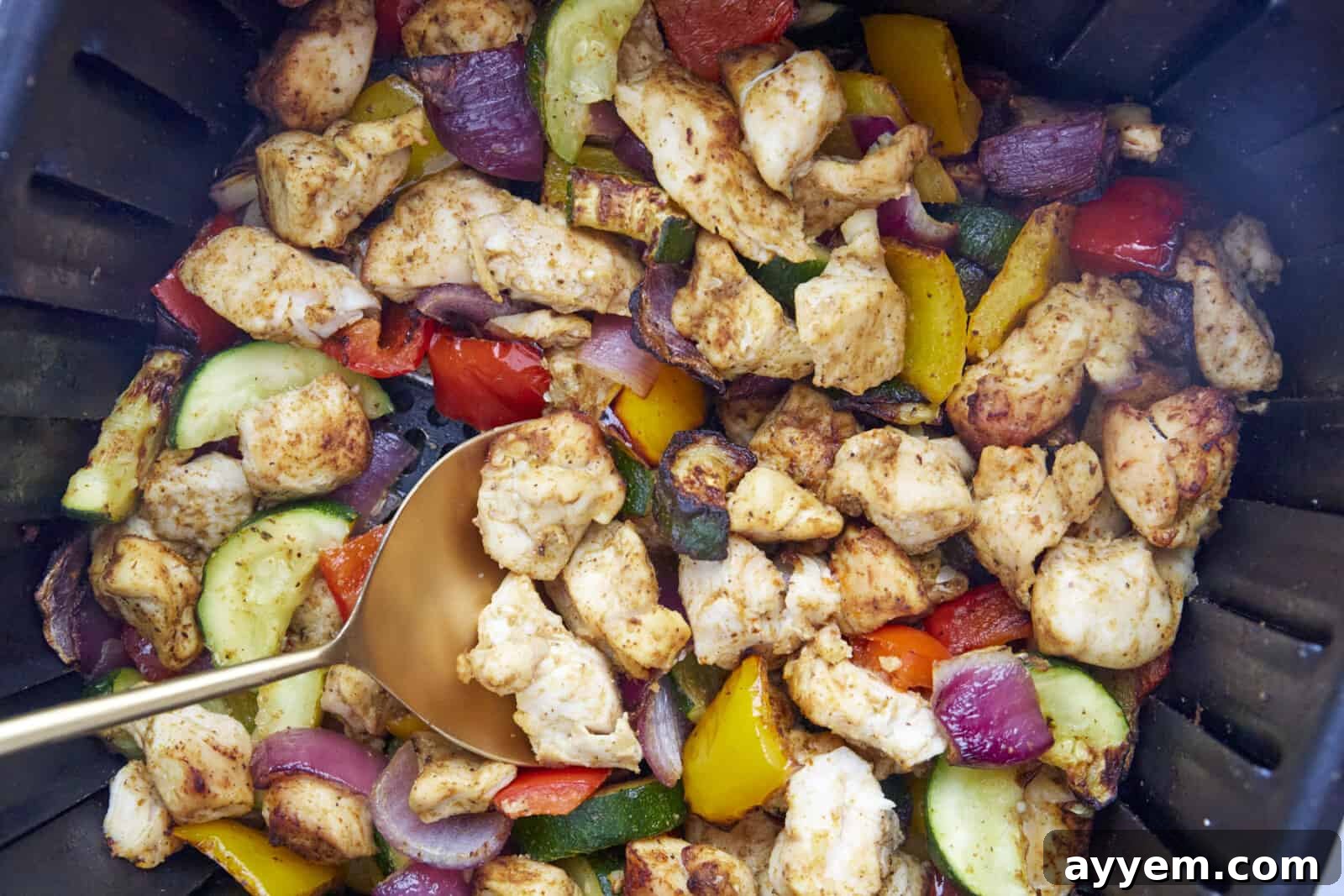 Close-up of cooked chicken and brightly colored vegetables perfectly roasted in an air fryer basket.