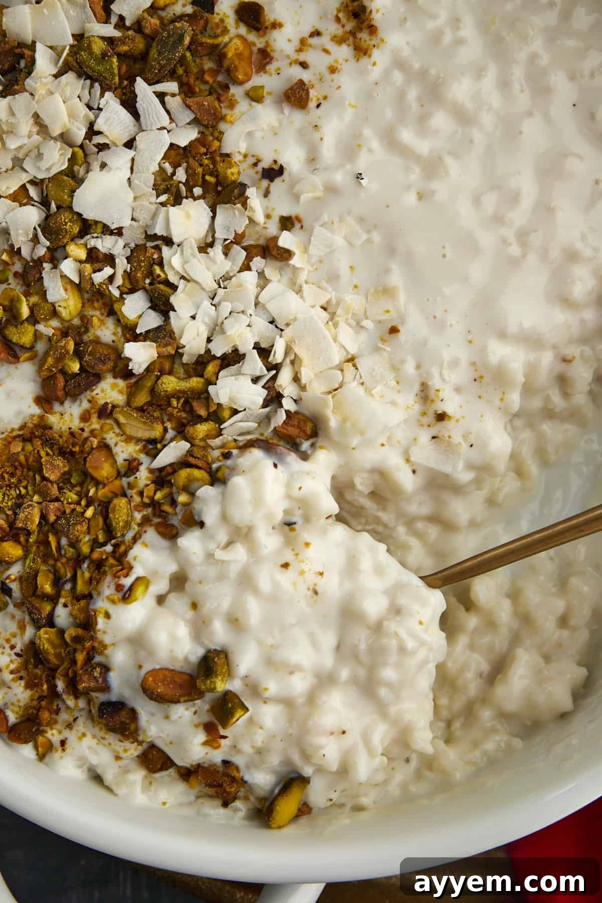 Close up image of a spoon scooping up coconut rice pudding topped with pistachios and coconut flakes