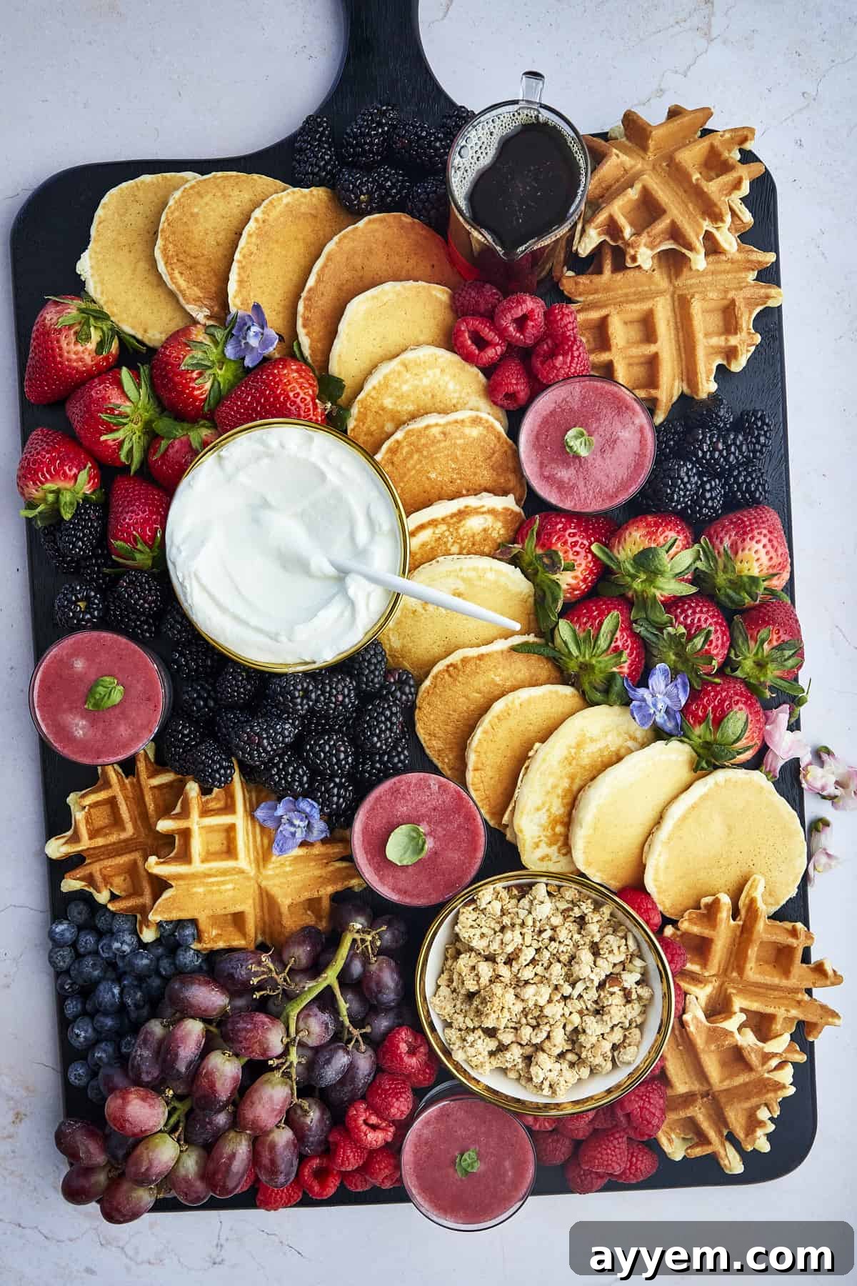 An overhead shot of a large and inviting breakfast charcuterie board, abundant with a variety of breakfast items, fruits, and small bowls of dips and syrups, ready for serving.