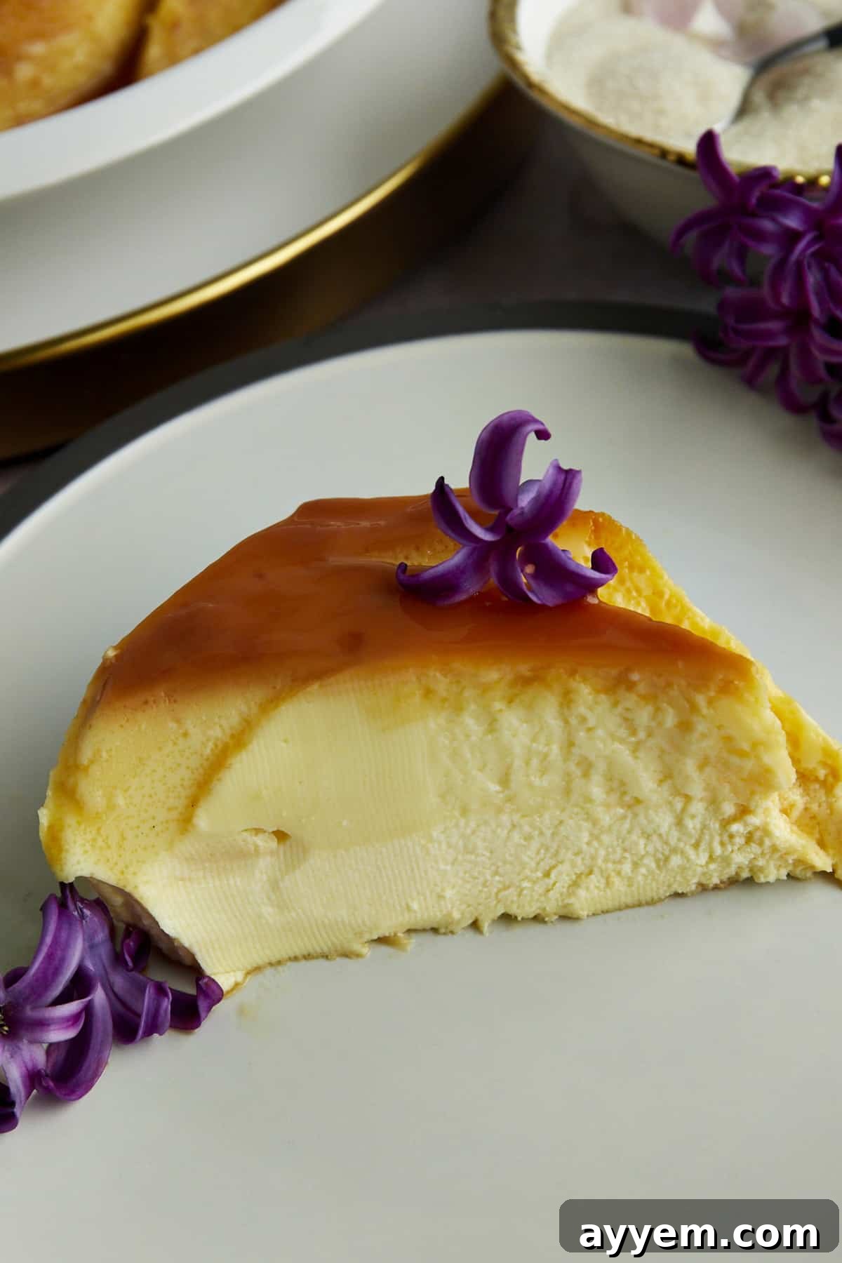 Side view of a generous slice of creme caramel, revealing its smooth texture and flowing caramel sauce on a white plate.