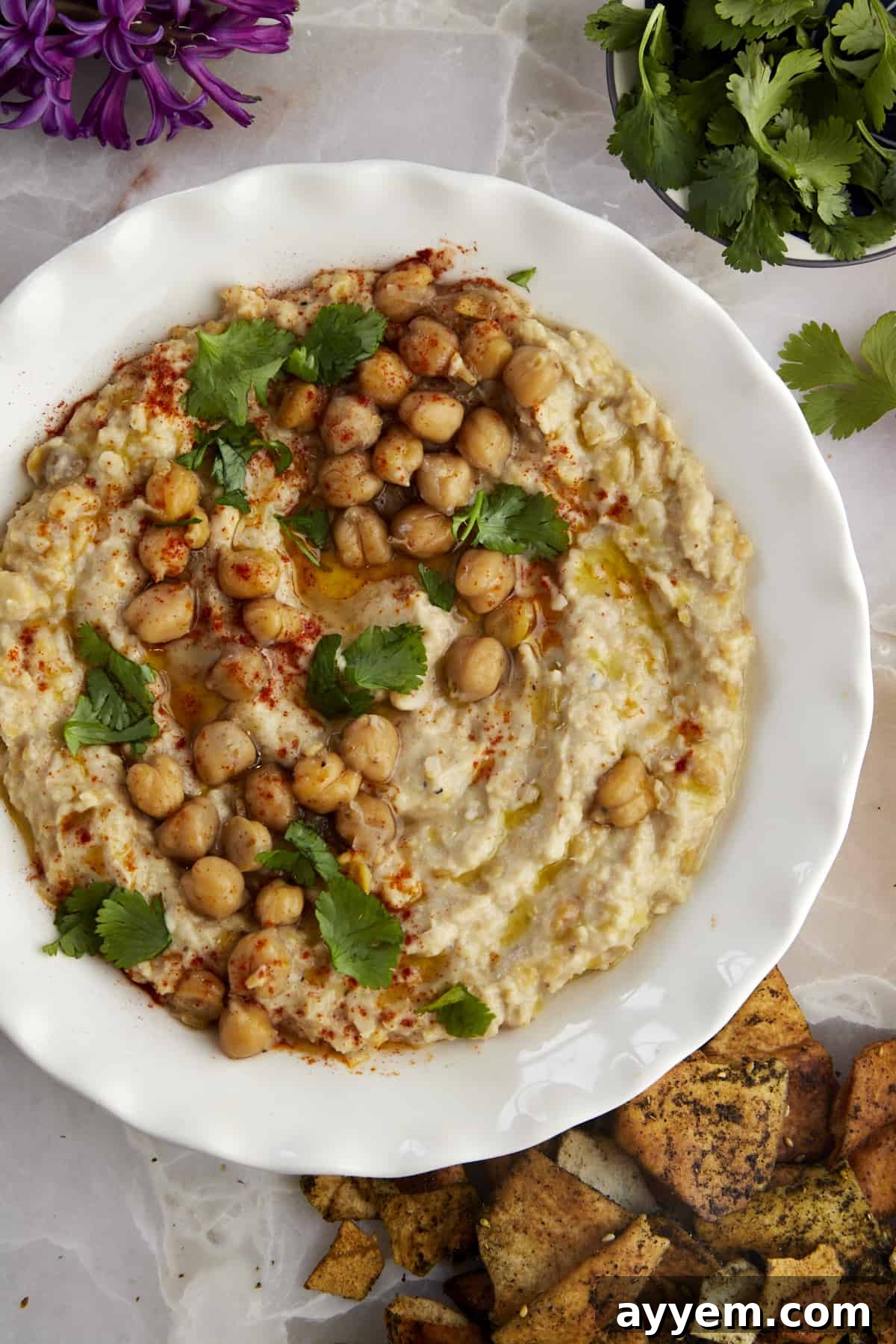 A bowl of chunky garlic hummus (Masabaha) garnished with whole chickpeas, parsley, and a drizzle of olive oil, ready for dipping.