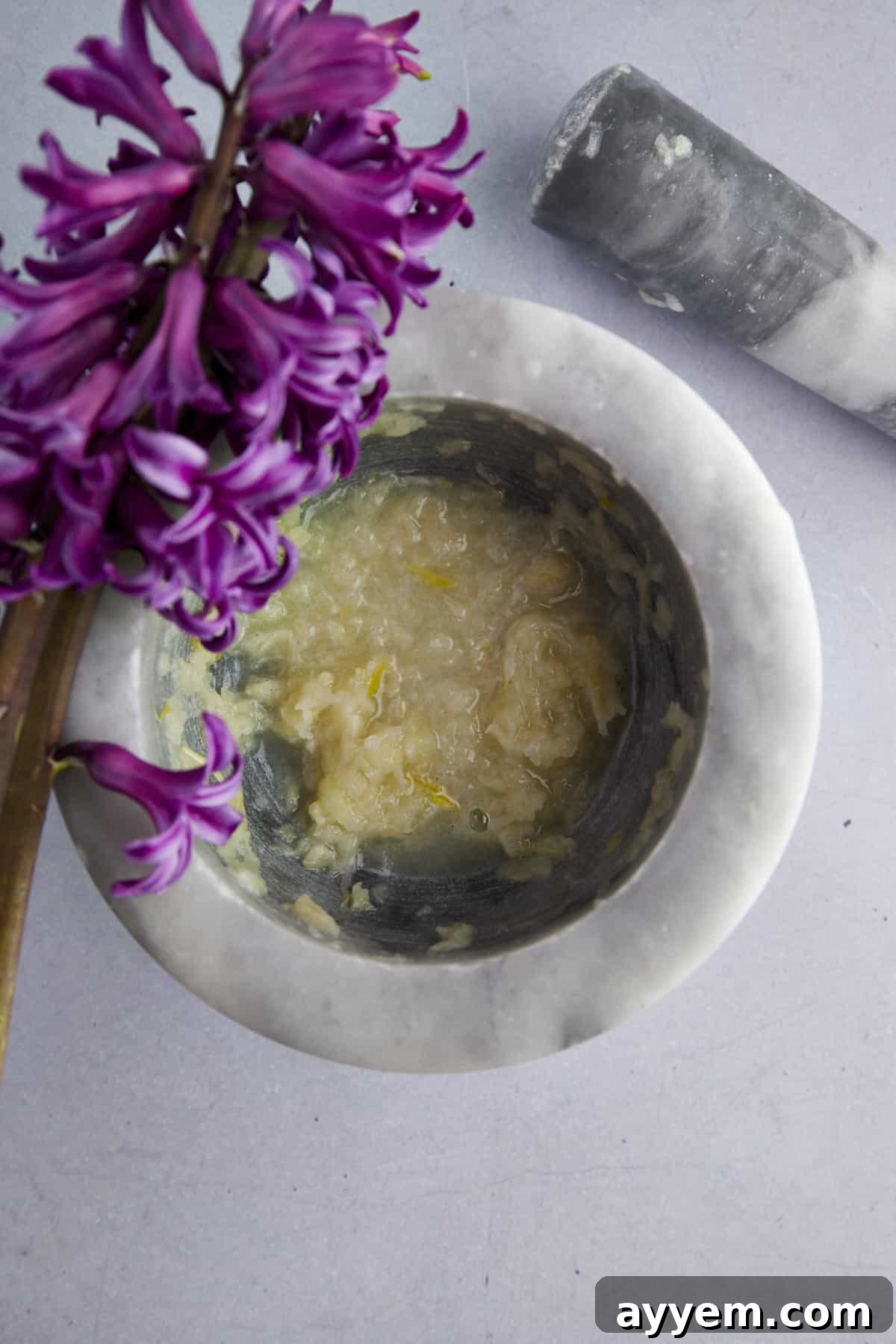 Fresh garlic cloves being crushed in a mortar and pestle, showcasing the traditional method of preparing the garlic paste for hummus.