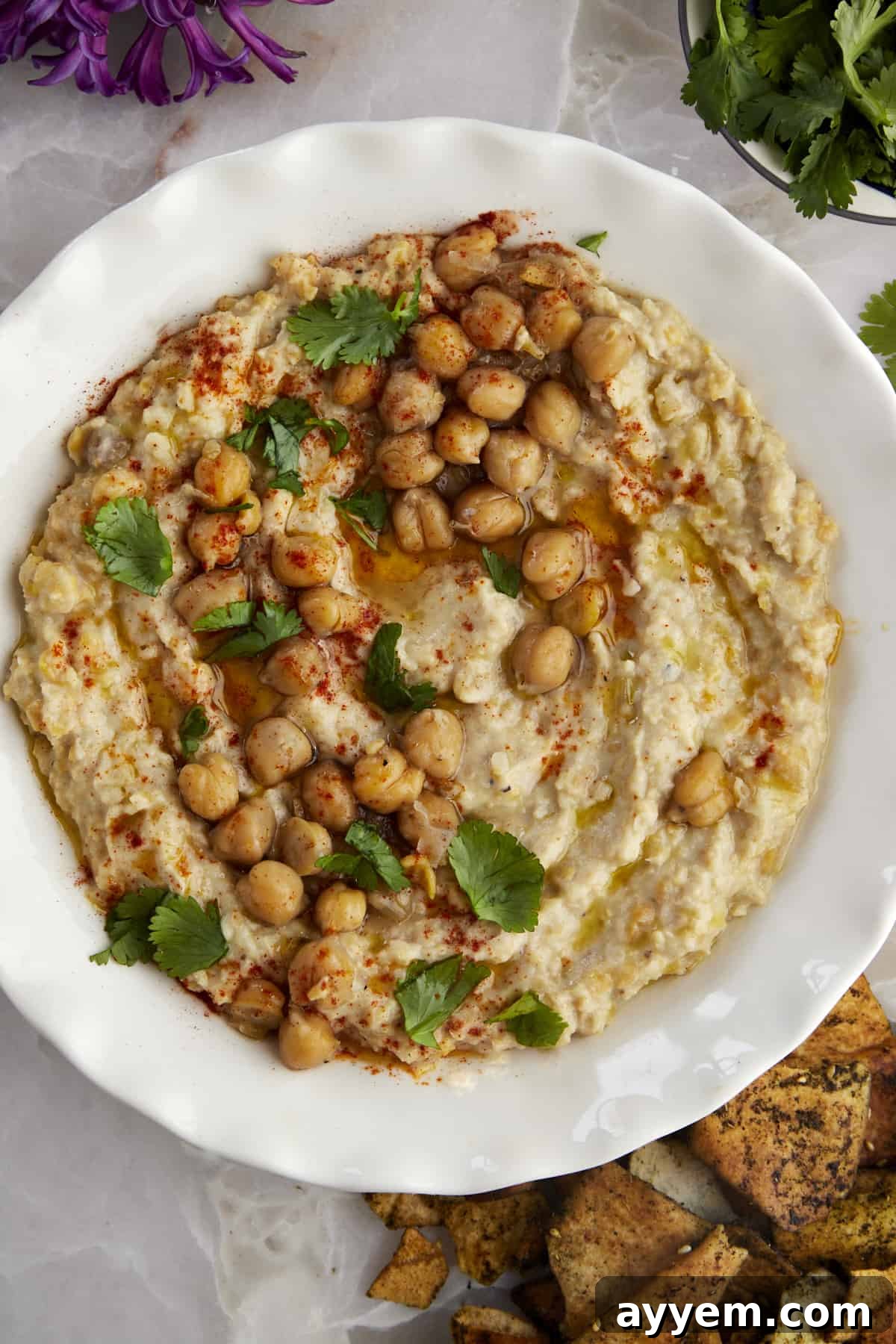 A close-up shot of chunky garlic hummus (Masabaha) in a bowl, showing its rustic texture and vibrant color, ready to be enjoyed with dippers.