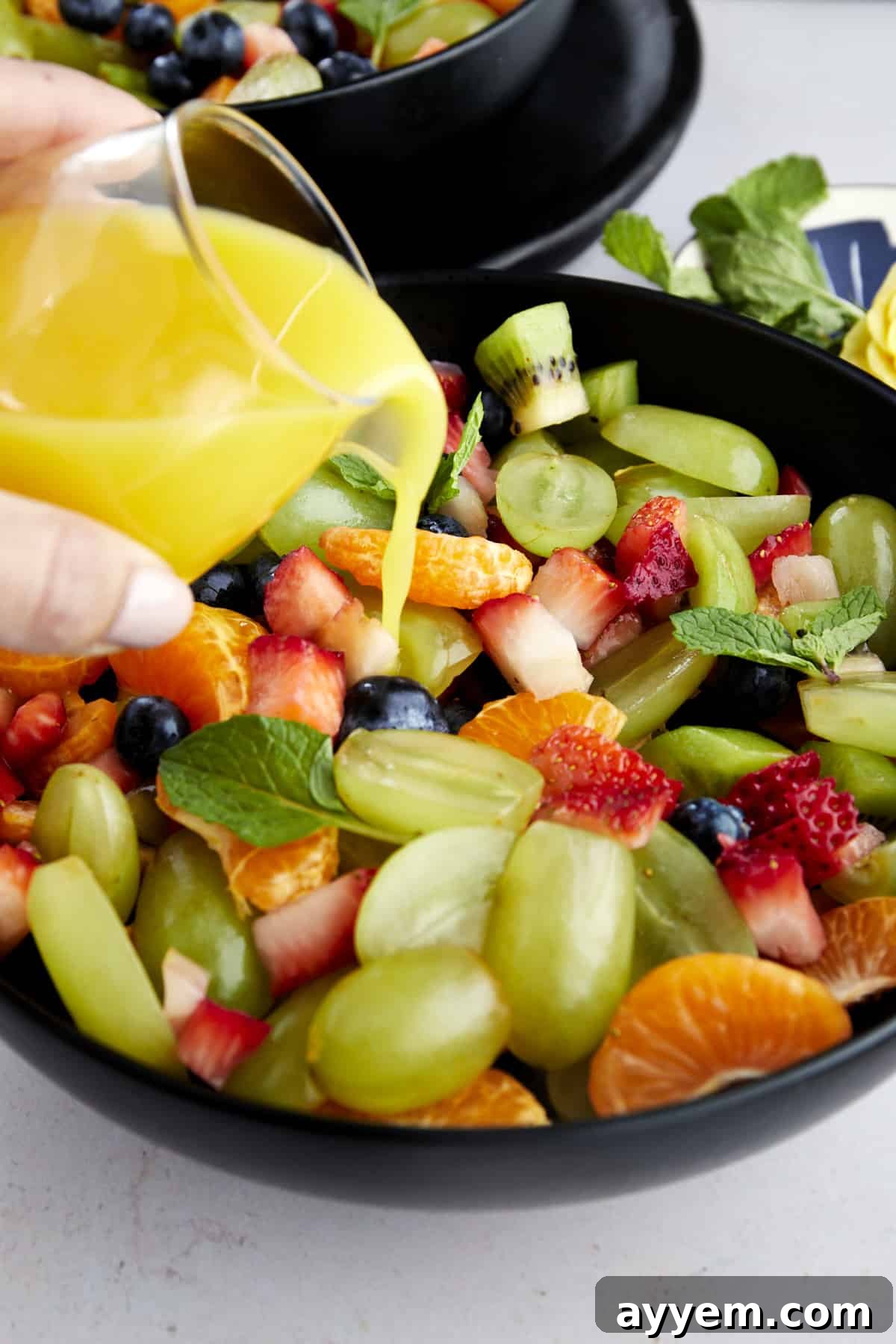 orange juice dressing being poured over a bowl of easy fruit salad